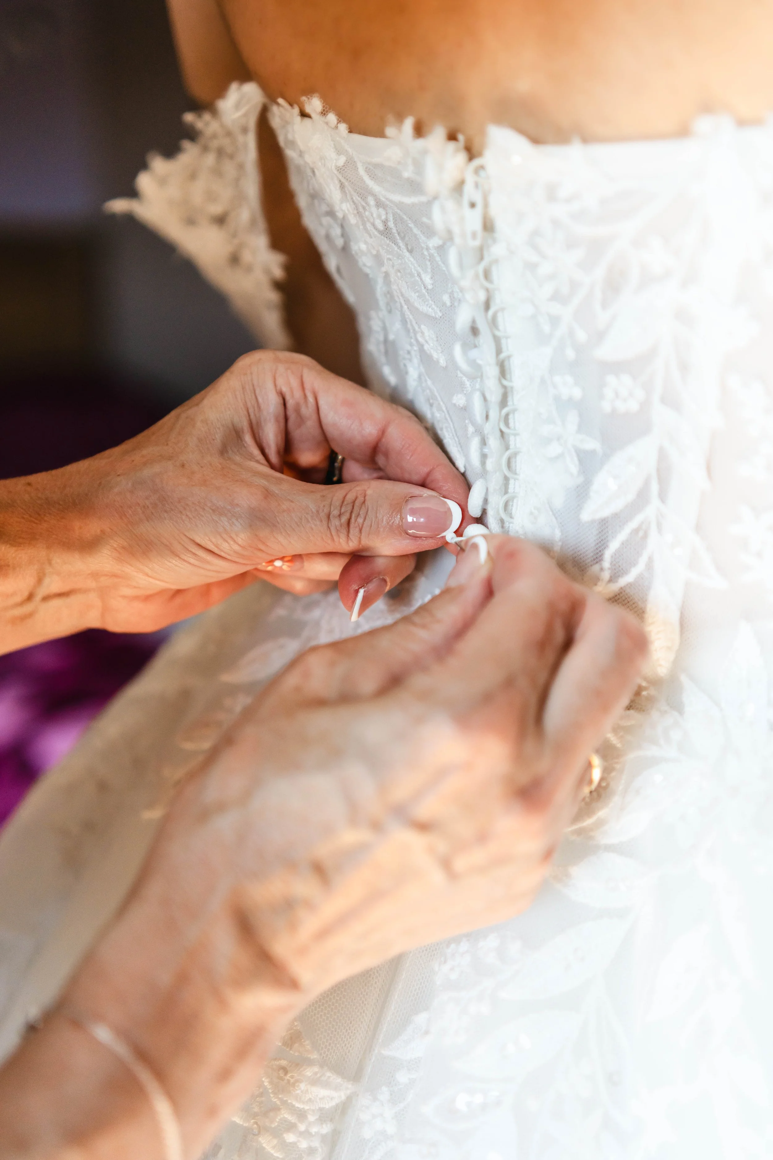 Une femme ajuste le bouton de la fermeture éclair d'une robe de mariée blanche en dentelle.
