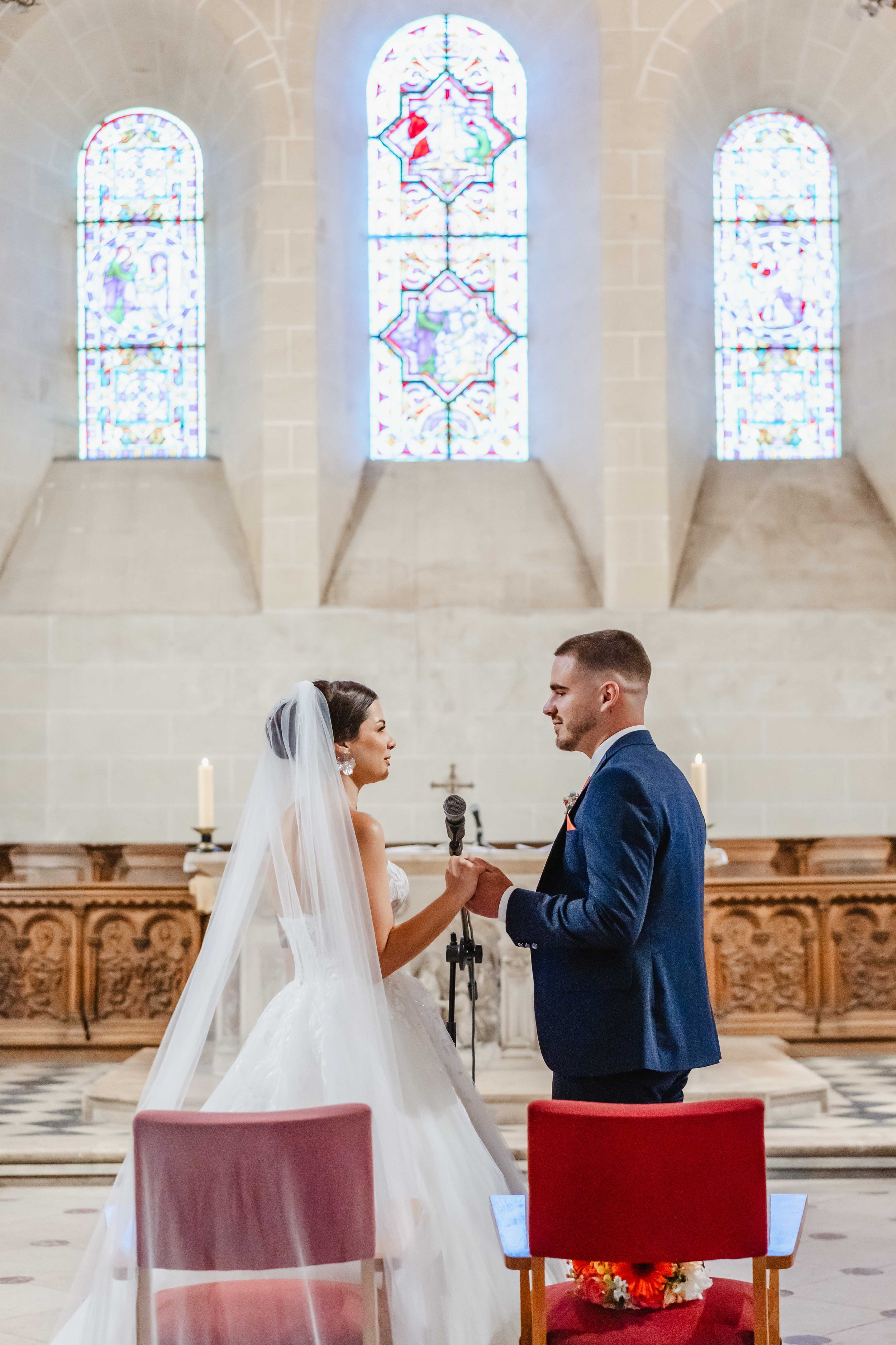 Un couple de mariés lors de leur mariage civil dans l'église de Saint Pierre Les Neymours avec des vitraux colorés en arrière-plan.