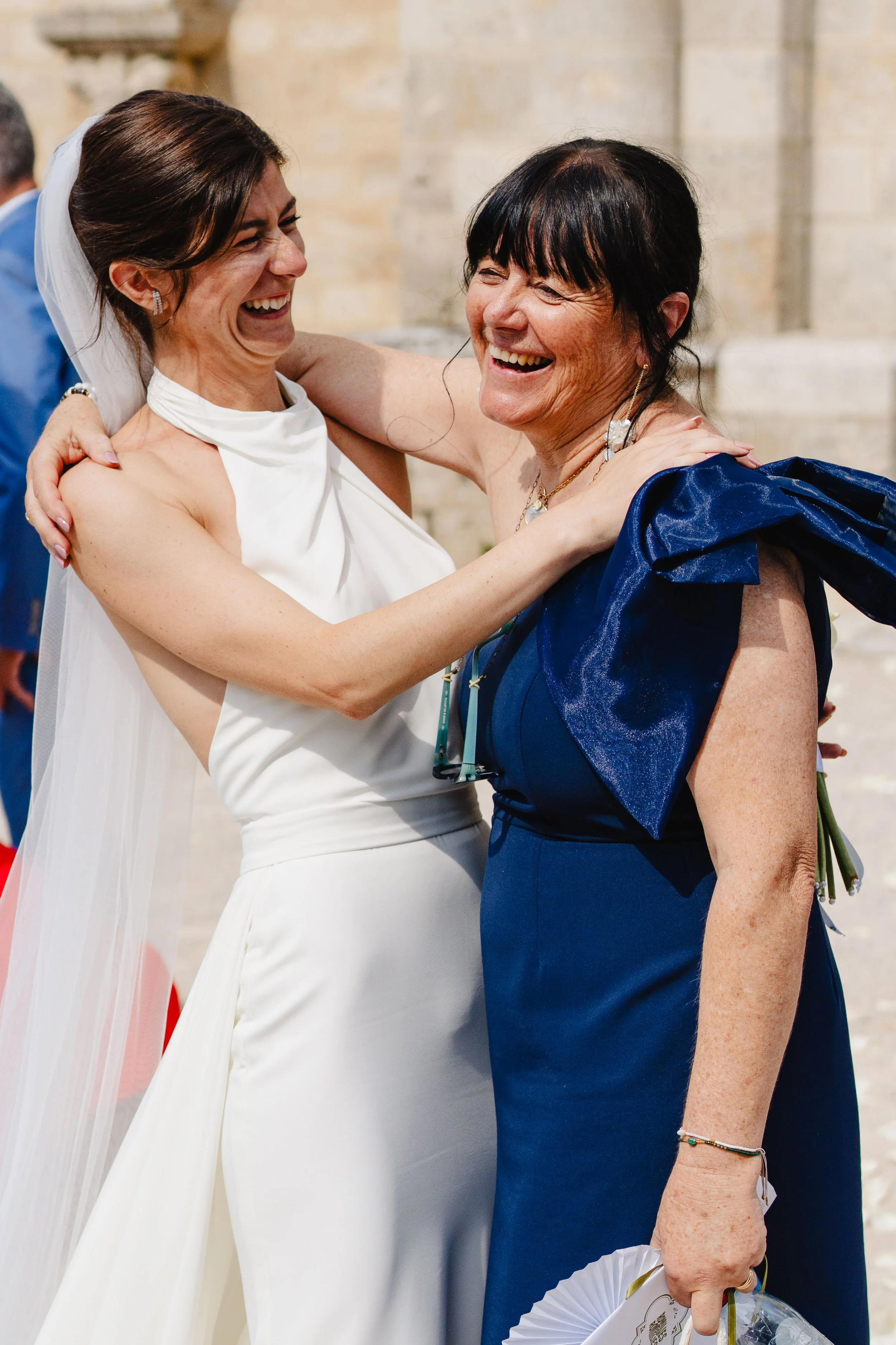 Deux femmes souriantes en costume de mariage lors d'une célébration, s'étreignant et riant ensemble.