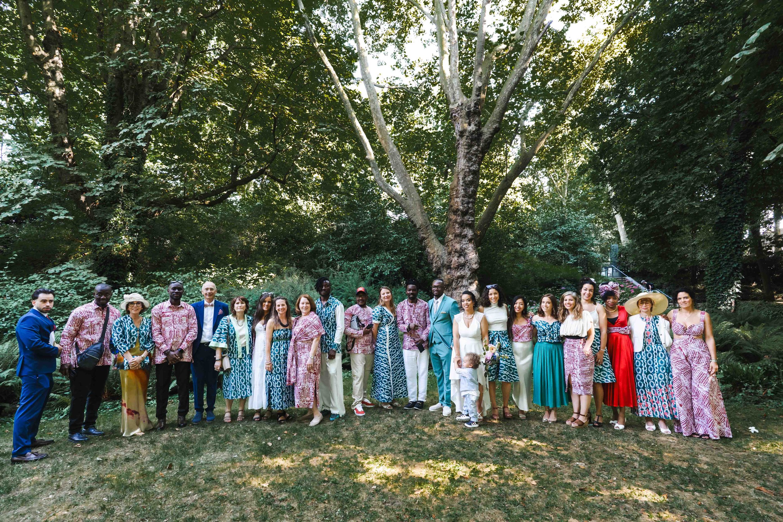 Groupe de personnes devant un grand arbre en forêt, certains en tenues colorées, d'autres en costume ou robe