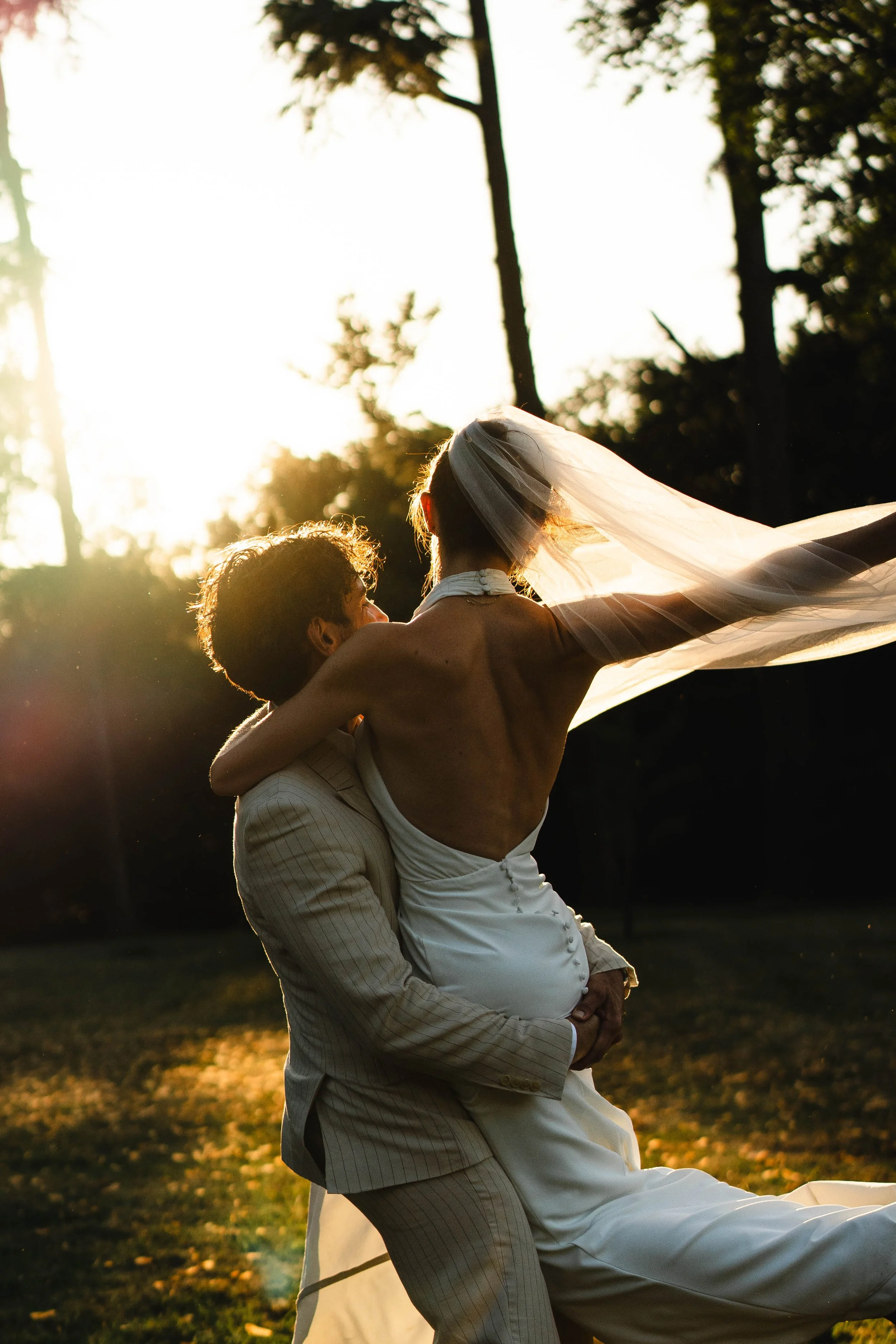 Un couple en mariage partage un moment romantique dans un cadre en plein air au coucher du soleil, avec des arbres en arrière-plan.