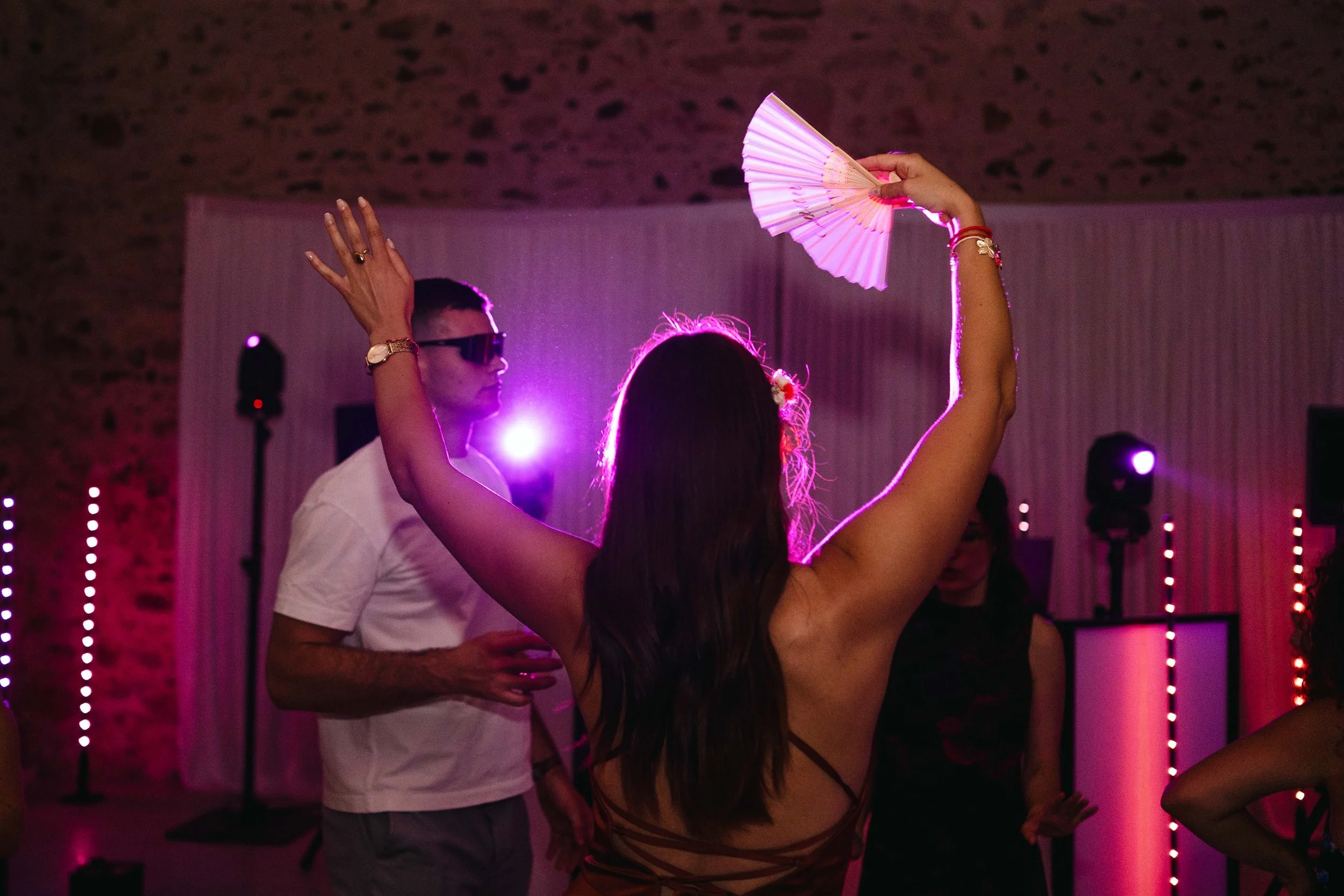 Une femme danse avec un éventail dans une ambiance de fête avec des lumières colorées.