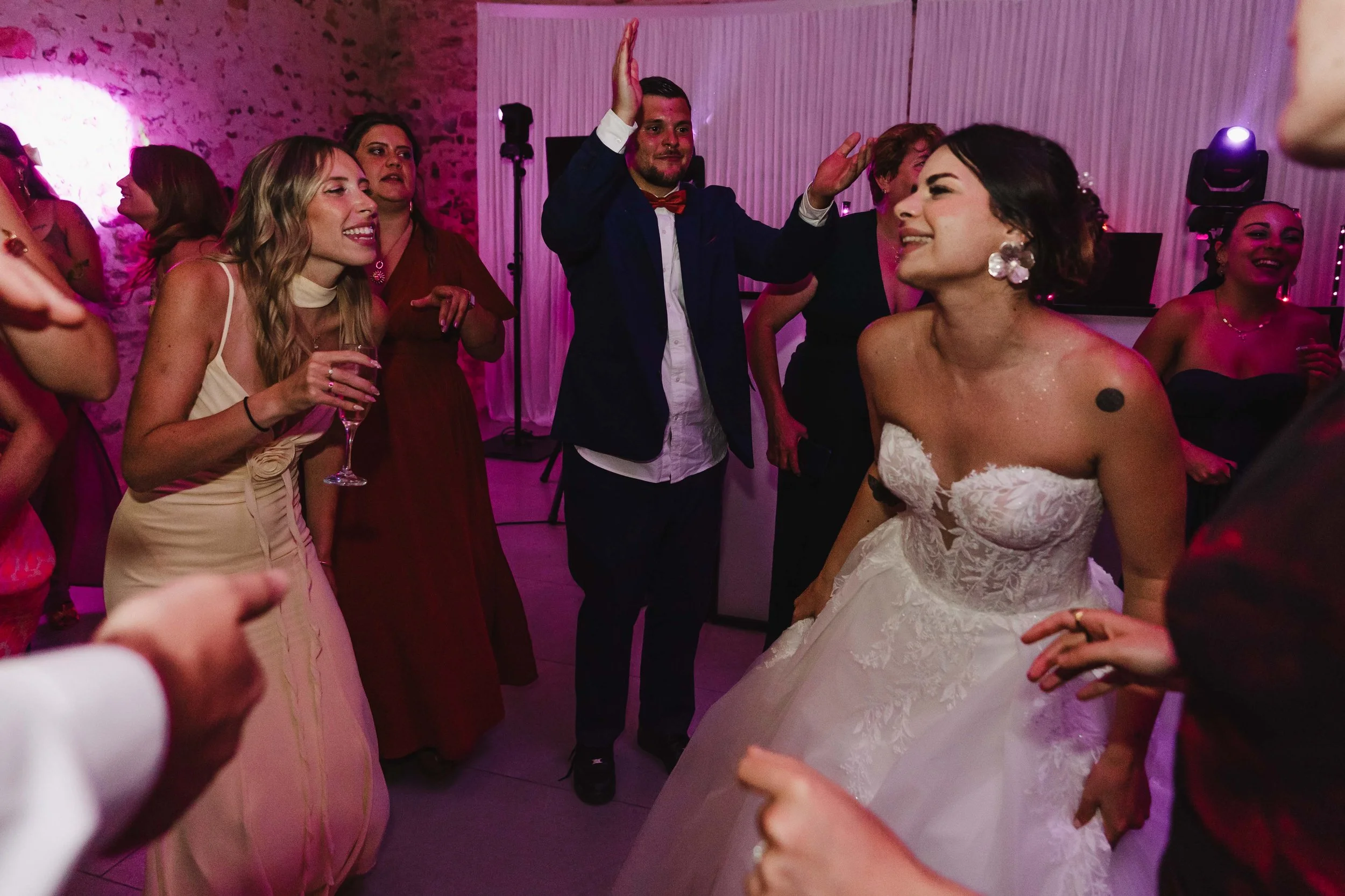 Groupe de personnes dansant et s'amusant lors d'un mariage, avec la mariée en robe blanche au centre.