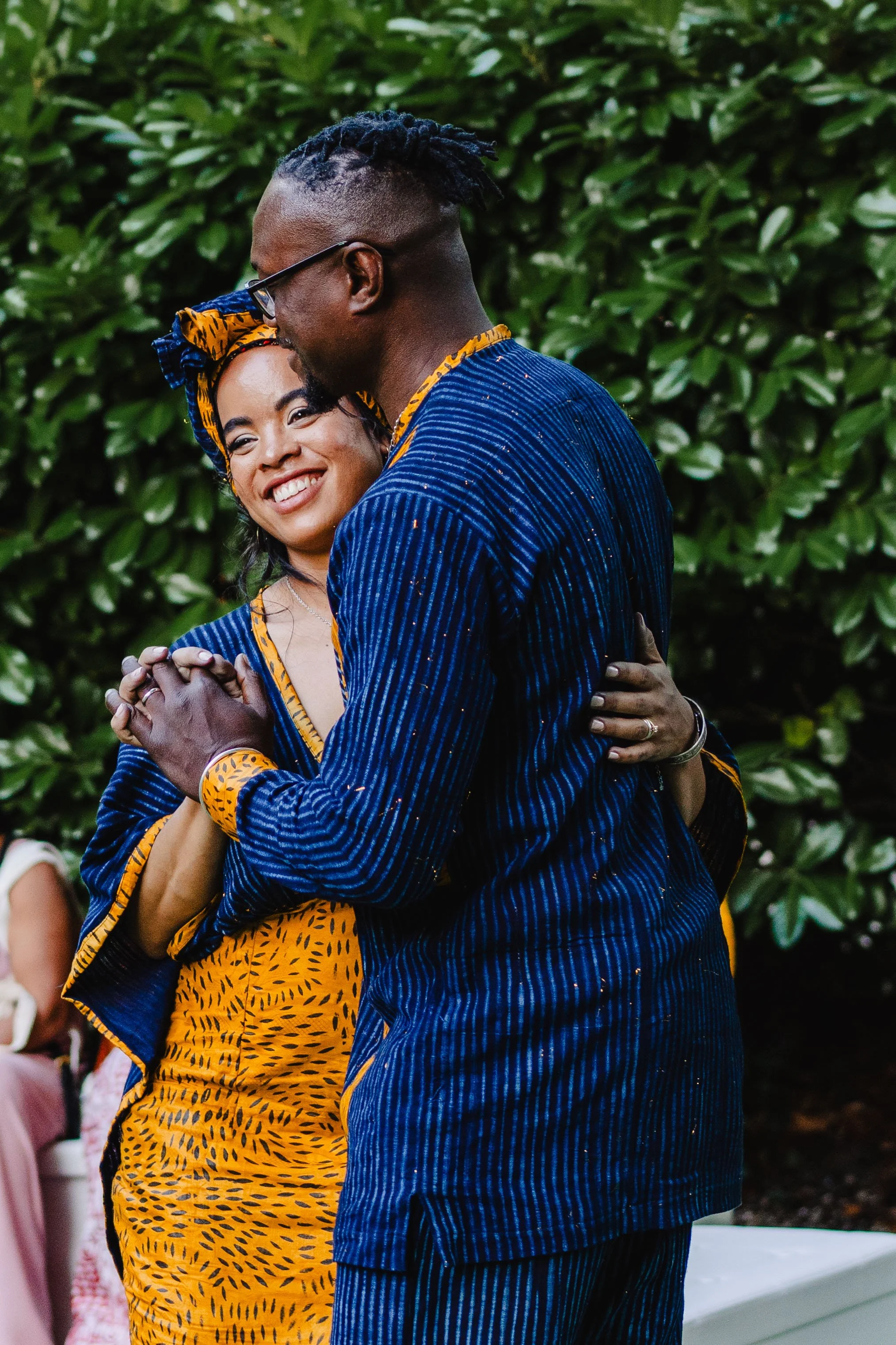 Un couple danse lors d'une cérémonie en pleine nature, habillés de vêtements colorés en tissu traditionnel avec motifs africains, partageant un moment de bonheur.