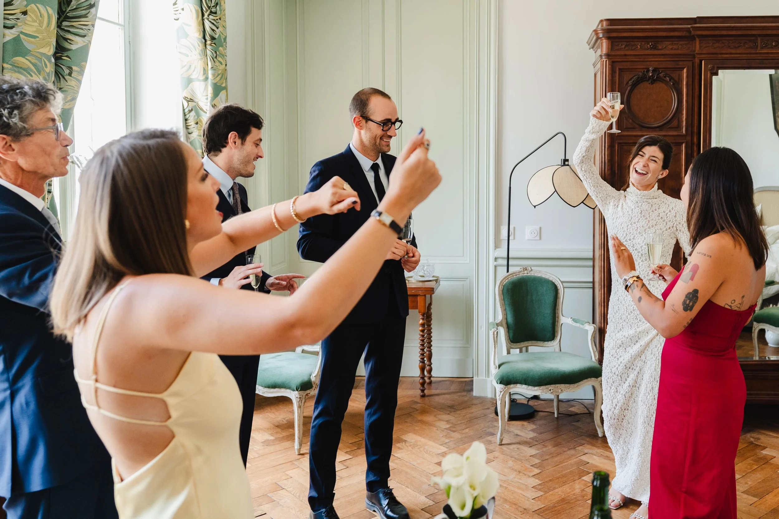 Groupe de personnes en tenue élégante, célébrant avec des verres de champagne dans une pièce bien décorée, souriants et heureux.