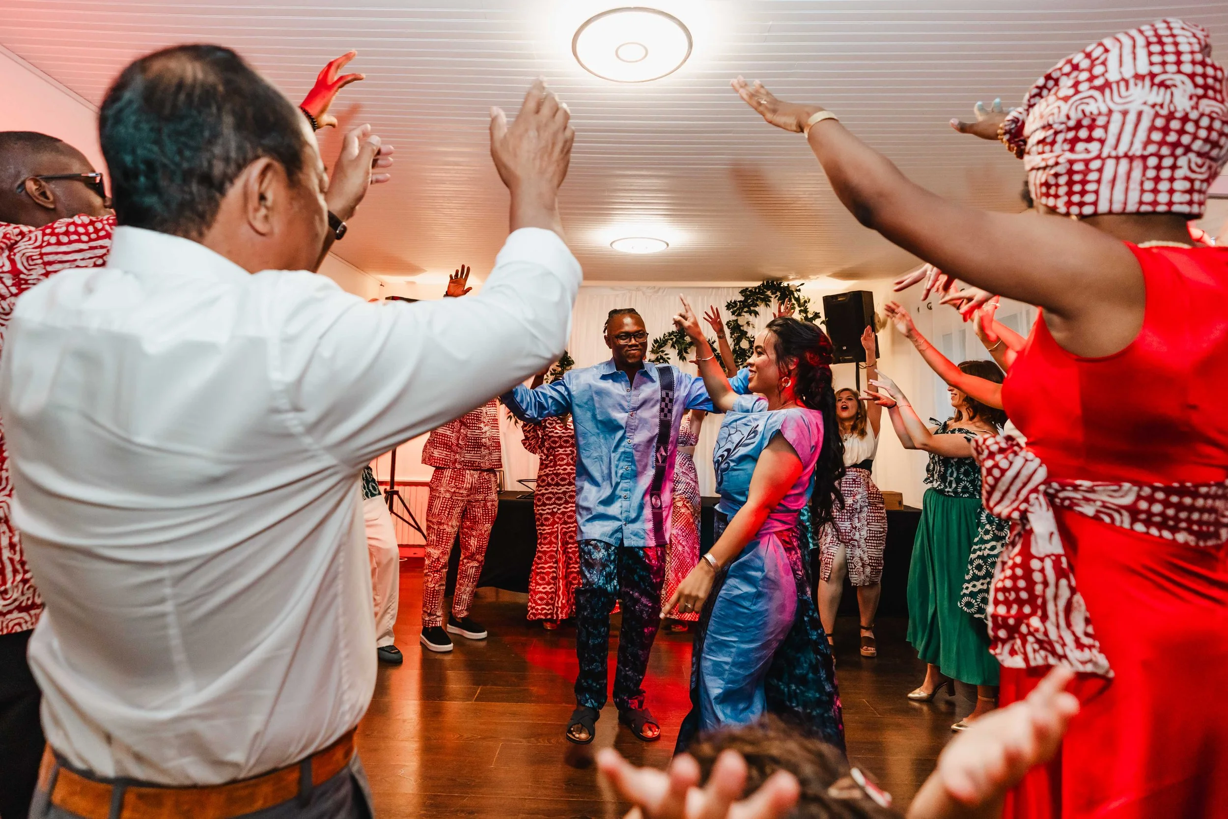 Groupe de personnes dansant lors d'une célébration ou fête, portant des vêtements colorés, dans une salle bien éclairée.