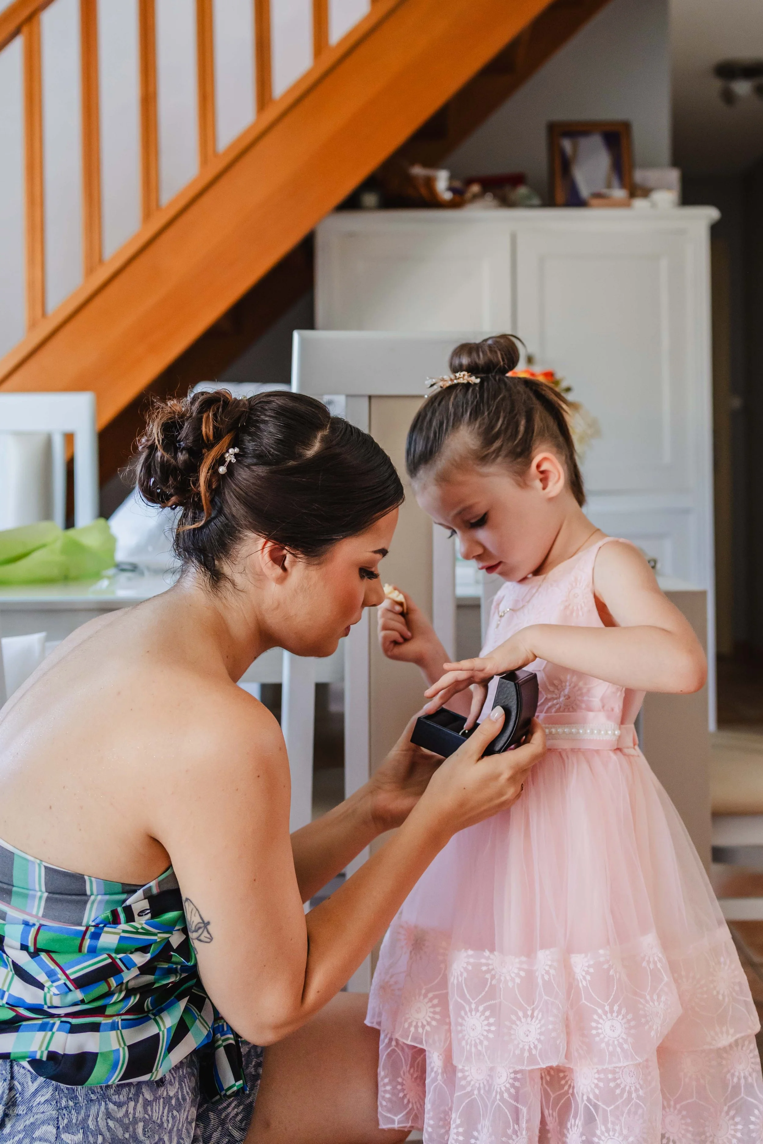 Une femme et une petite fille en robe rose, se préparant, probablement pour une occasion spéciale, dans une maison.