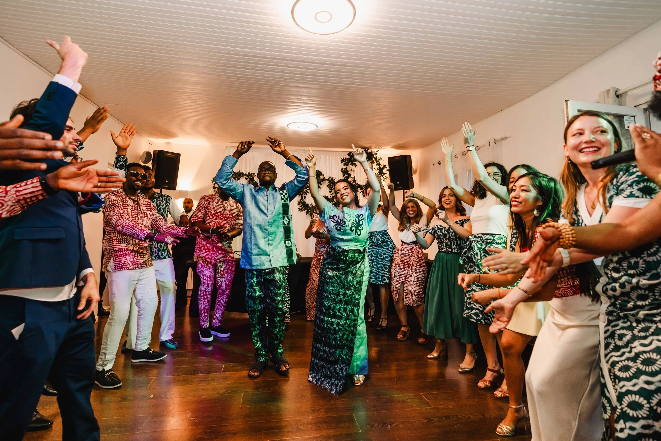 Groupe de personnes dansant et souriant lors d'une célébration ou d'une fête dans une pièce bien éclairée.