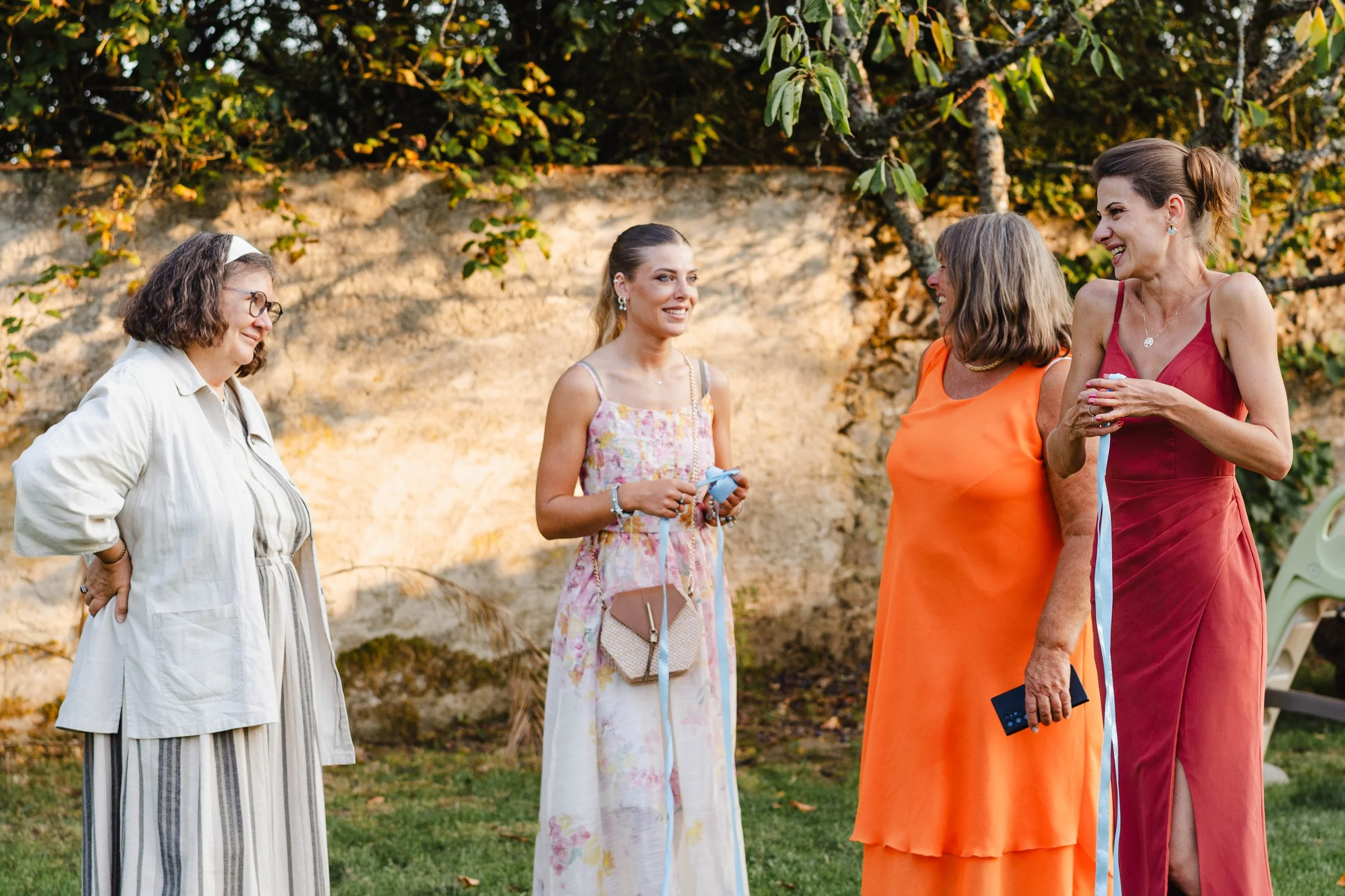Groupe de cinq femmes souriantes en conversation dans un jardin, portant des vêtements d'été colorés au domaine de Mauperthuis.