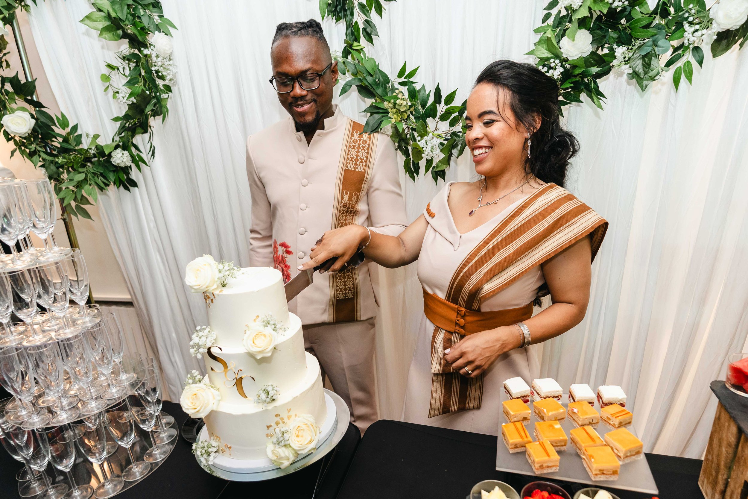 Un couple coupe un gâteau de mariage lors d'une célébration dans un décor floral blanc et vert.