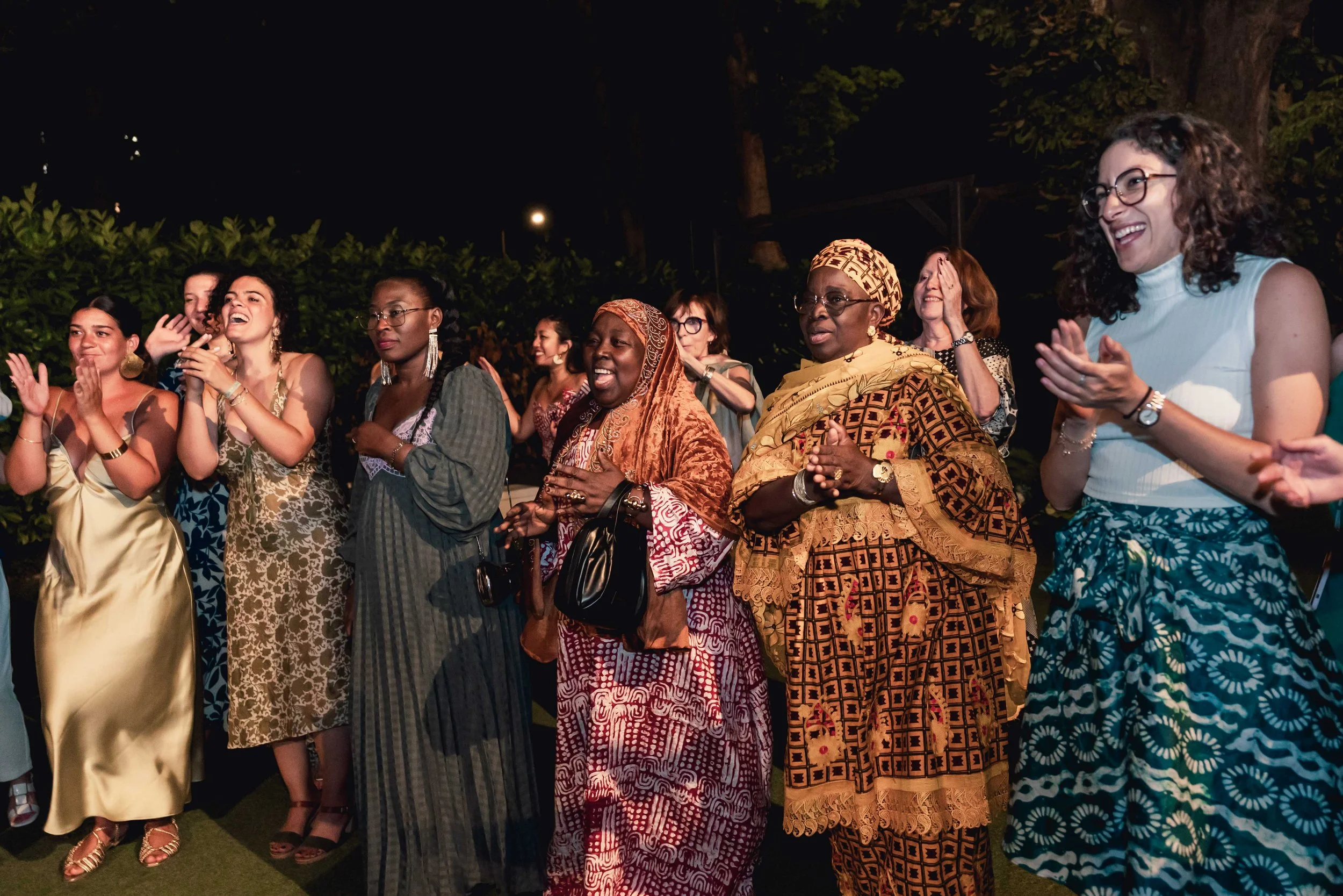 Groupe de femmes variées, souriantes, applaudissant lors d'une soirée en plein air au moulin vert.