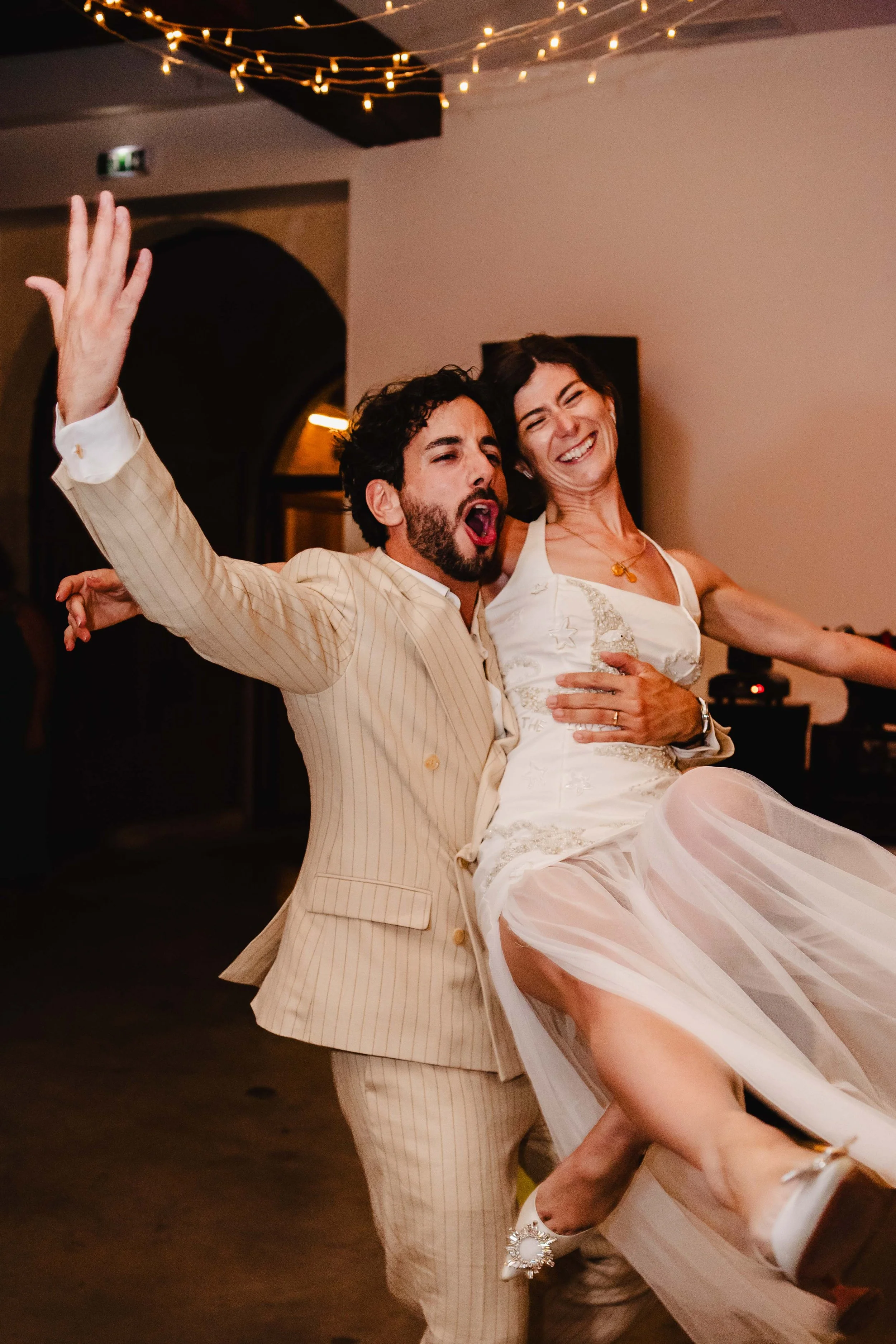 Un couple de mariés dansant et s'amusant lors de leur mariage dans la salle de réception du chateau Saint Denis, avec des guirlandes lumineuses au plafond.