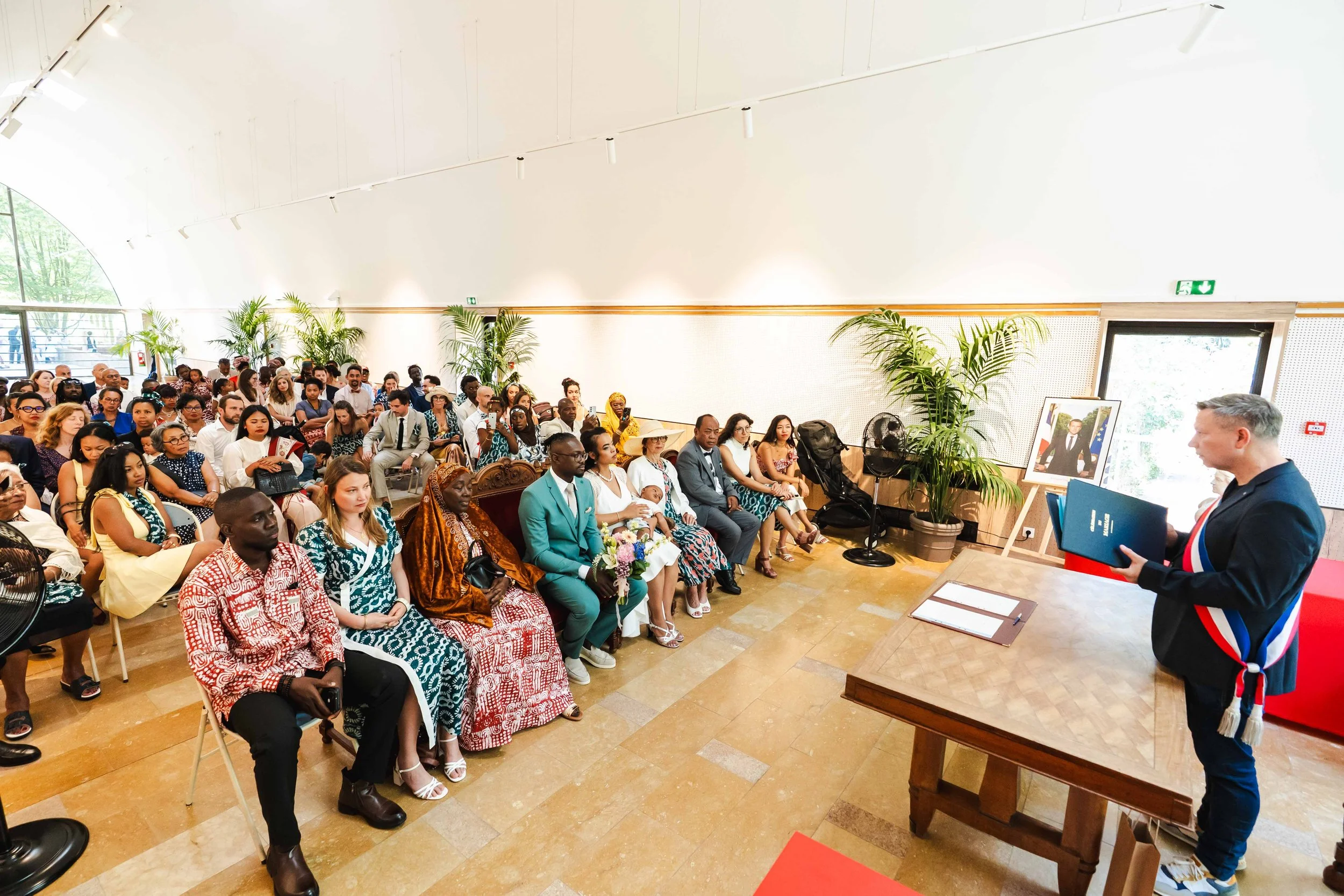 Une cérémonie officielle avec un orateur s'adressant à un public diversifié assis dans une salle bien éclairée.