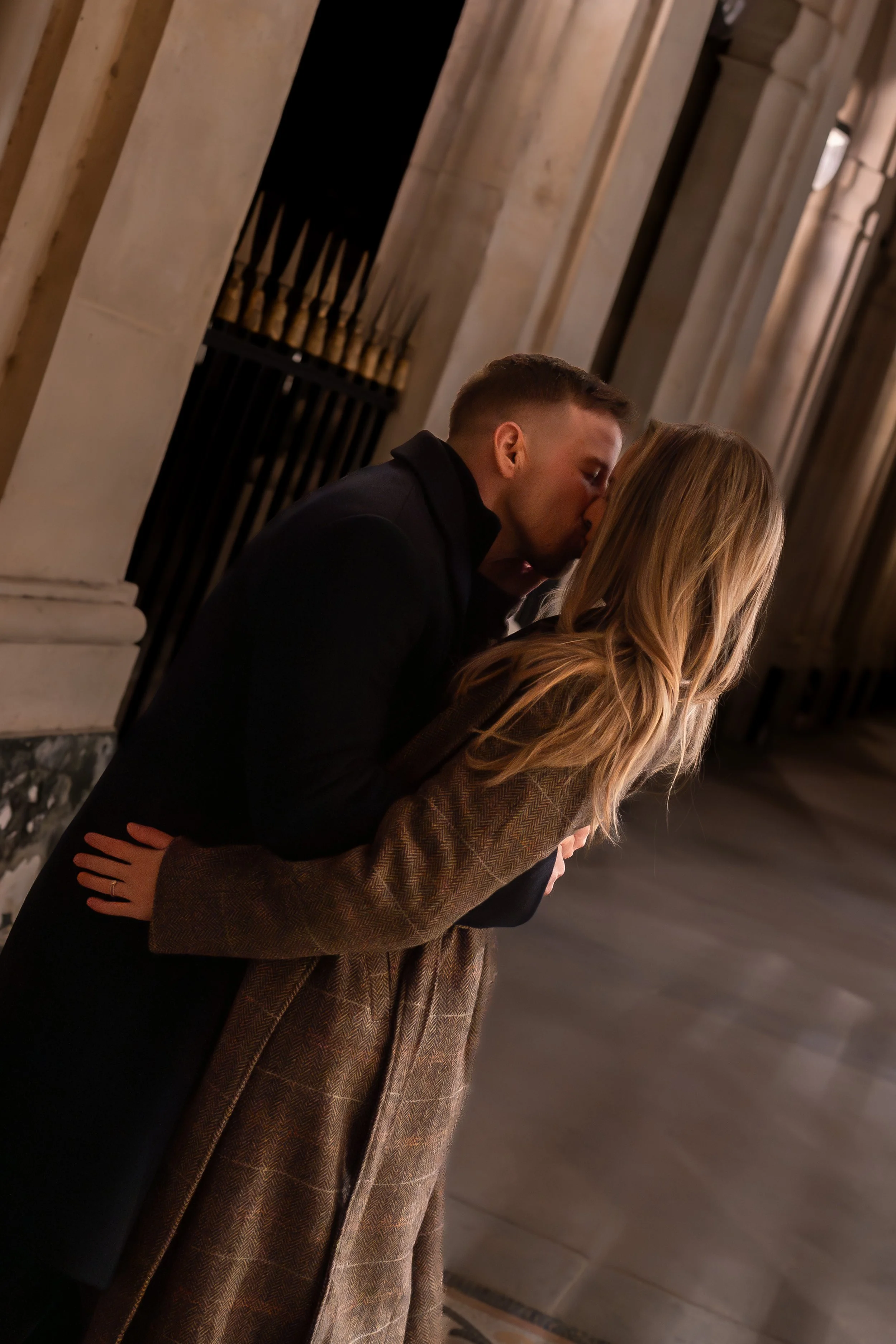 Un couple partage un baiser dans un couloir en pierre, probablement dans un bâtiment historique ou une cathédrale, au Palais Royal.