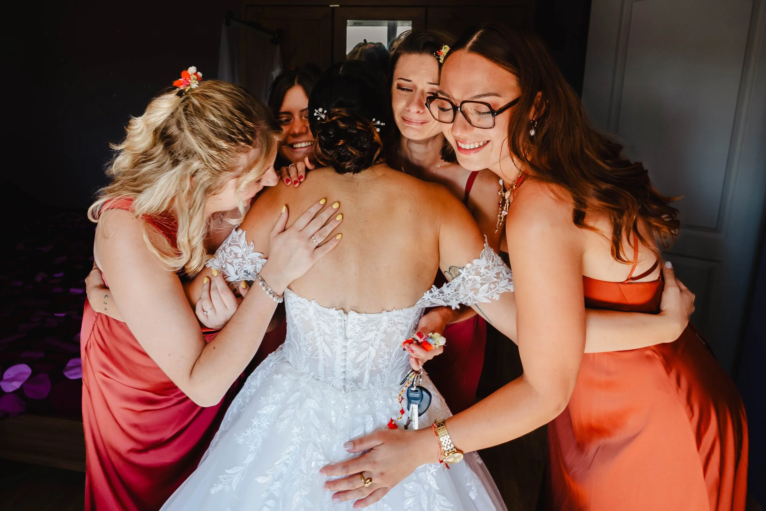 Un groupe de femmes en robe de cocktail rouge et en robe de mariée en train de faire un câlin, manifestant des émotions chaleureuses et de la joie.