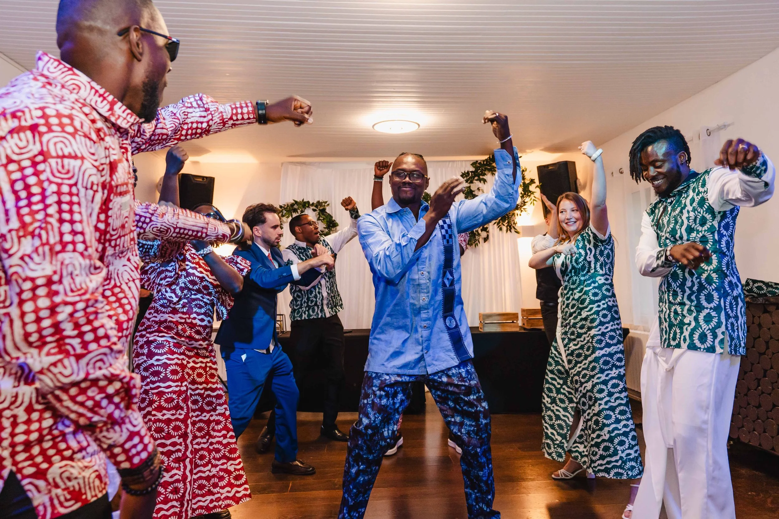 Groupe de personnes dansant joyeusement lors d'une fête à l'intérieur, habillées de vêtements colorés et modernes.