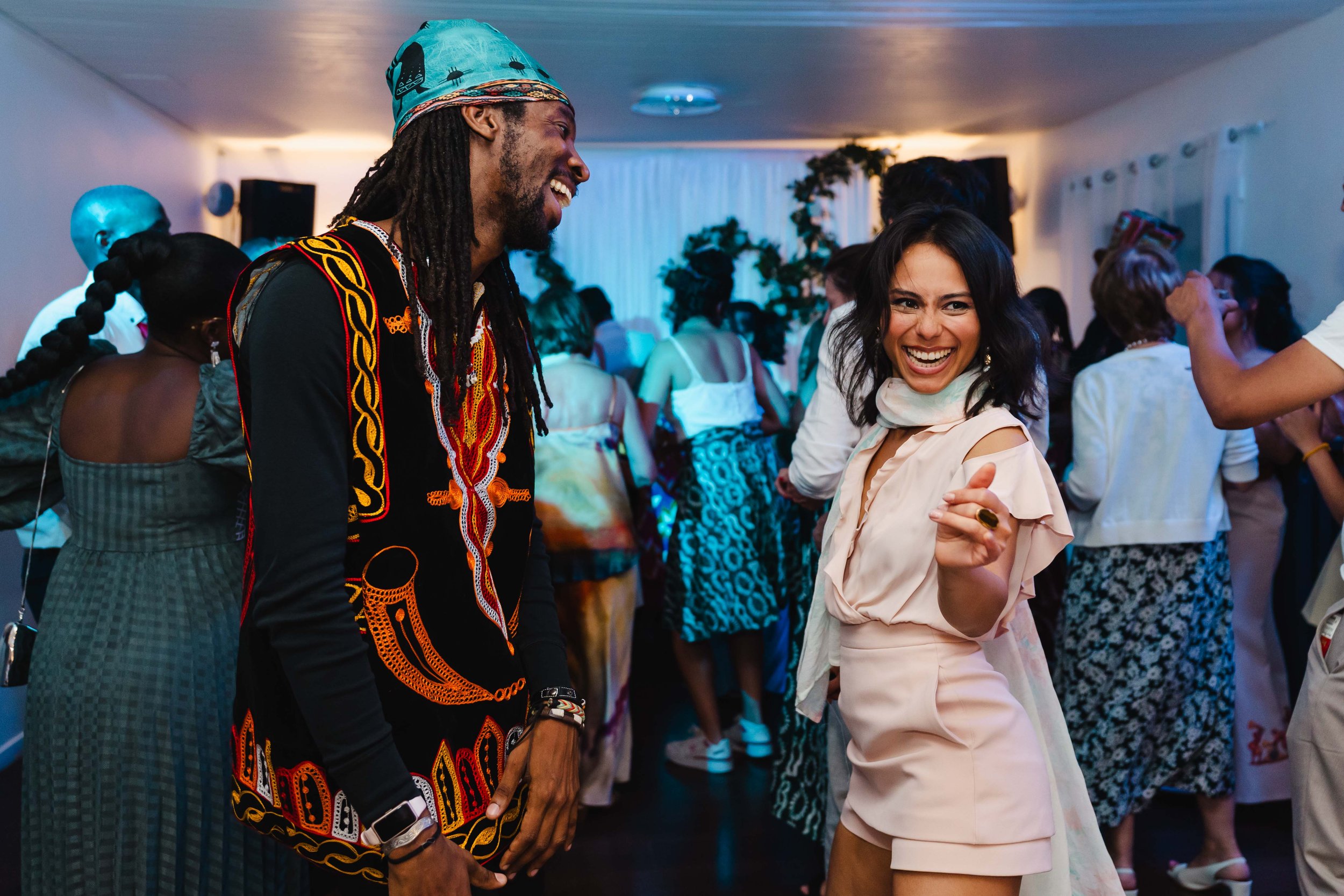 Deux personnes souriantes dansant lors d'une fête au Moulin vert à Champigny, un homme avec une chemise à motifs colorés et une femme en tenue claire, entourés d'autres invités au fond.
