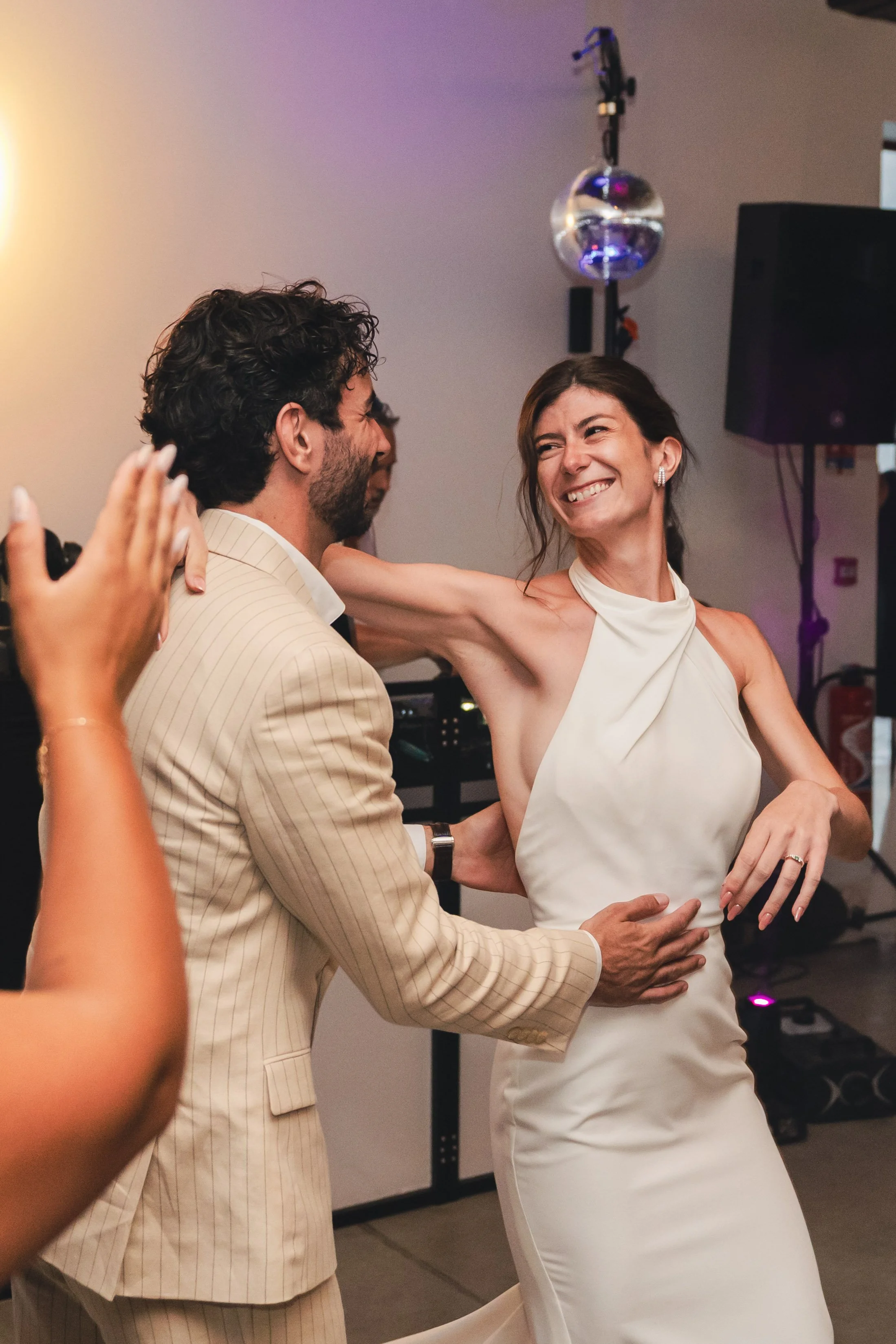 Un couple danse lors d'une célébration avec une femme en robe blanche souriante et un homme en costume beige.