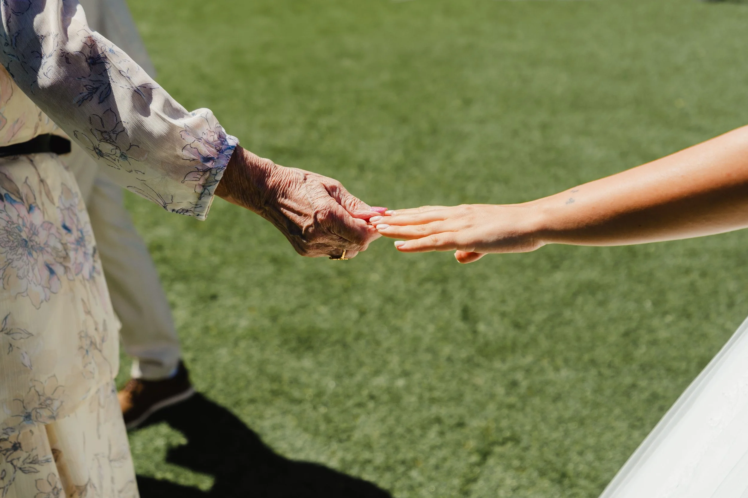 Une personne âgée tenant la main d'une jeune femme lors d'une cérémonie en plein air, avec un terrain vert en arrière-plan.