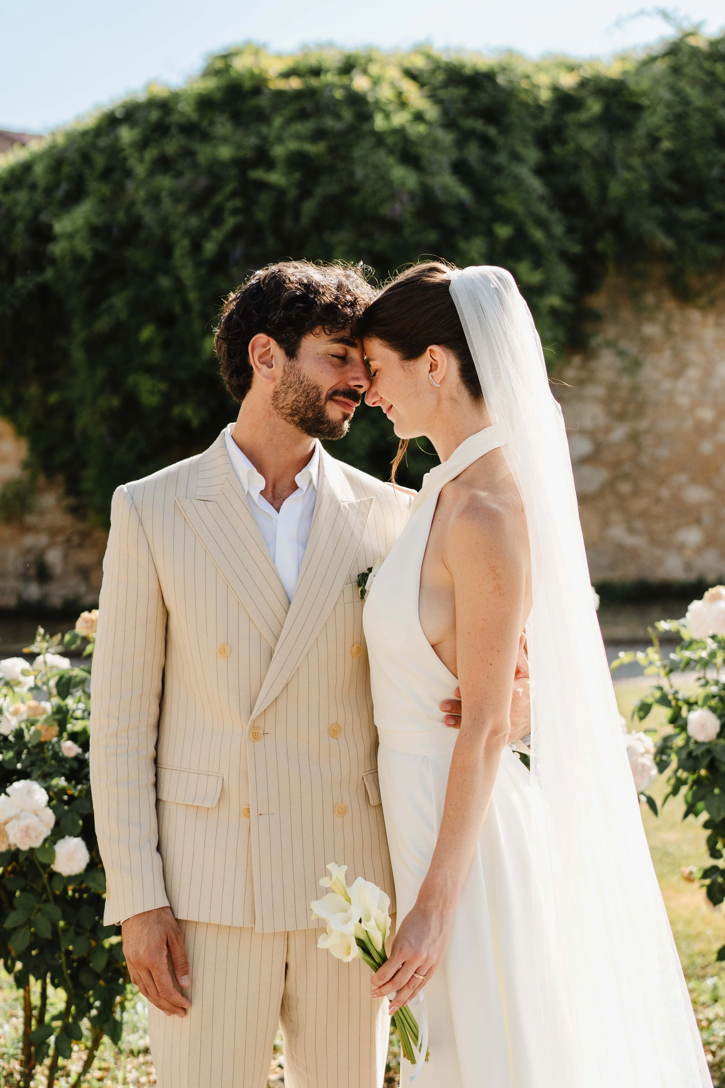 Un couple de mariés se touche le front lors de leur mariage en plein air, avec des roses en arrière-plan.