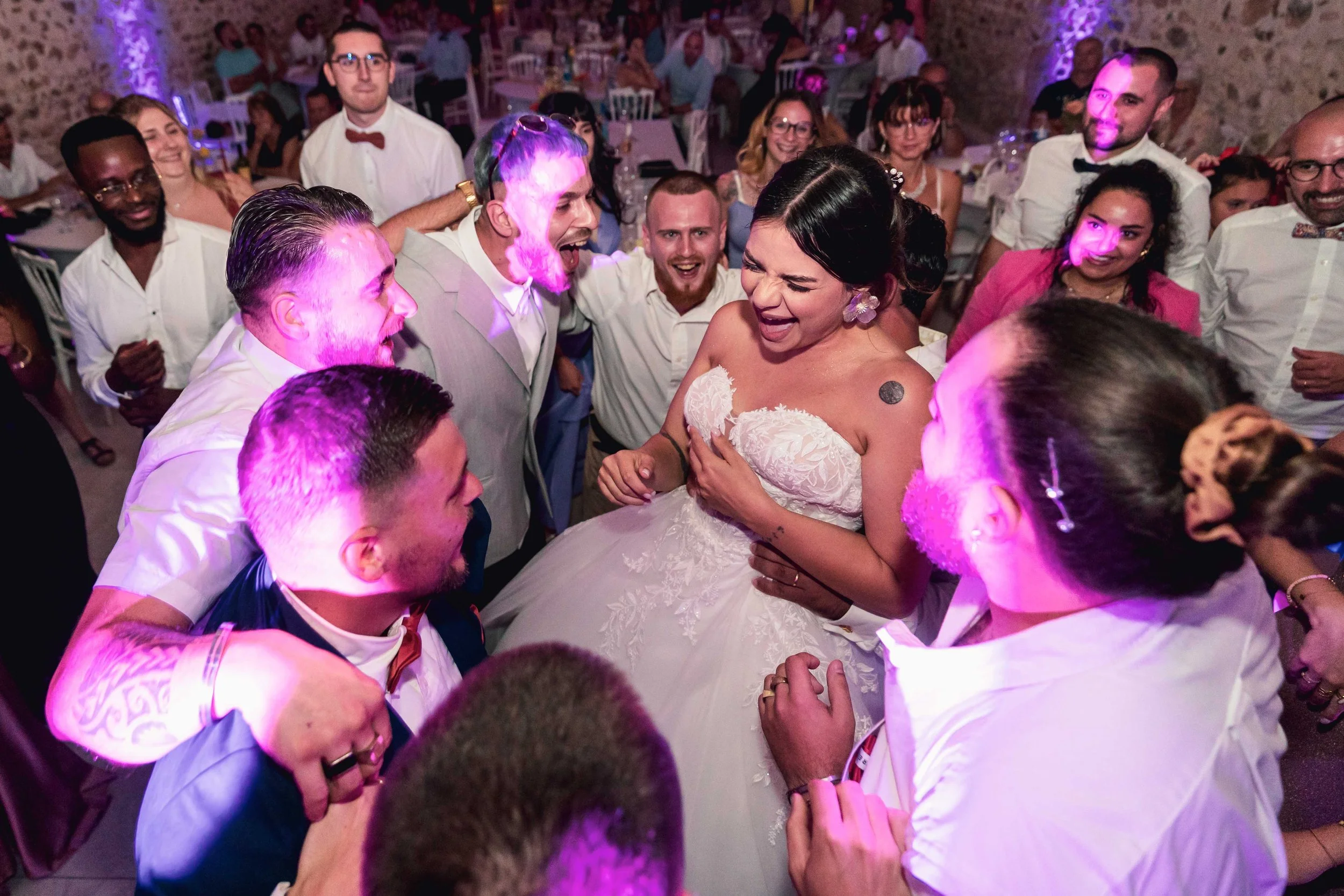 Mariage avec la mariée entourée d'amis qui dansent et rient, dans une salle décorée pour la fête.