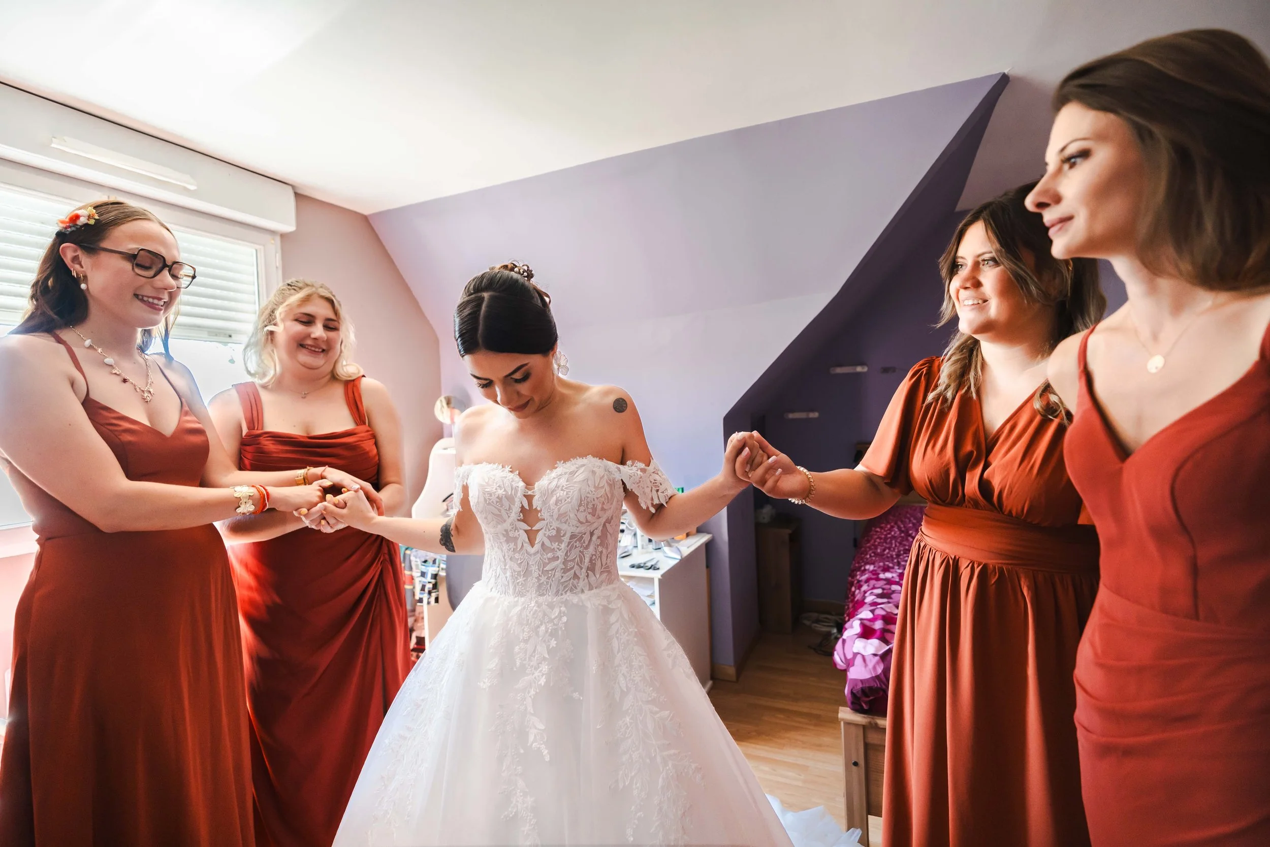 Fée de mariage en robe blanche entourée de cinq demoiselles d'honneur en robes marron, dans une pièce avec fenêtre.