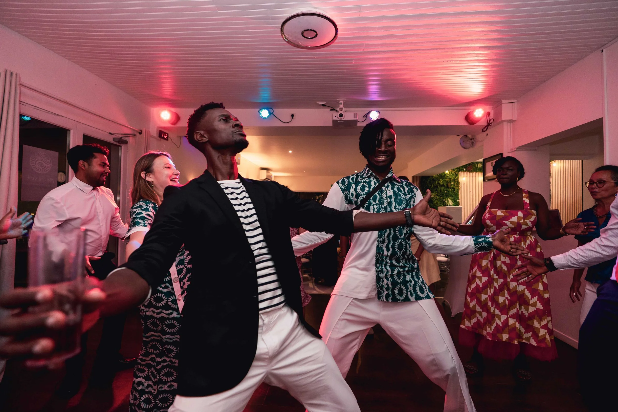 Groupe de personnes dansant et souriant lors d'une fête à l'intérieur, ambiance festive avec lumière colorée.