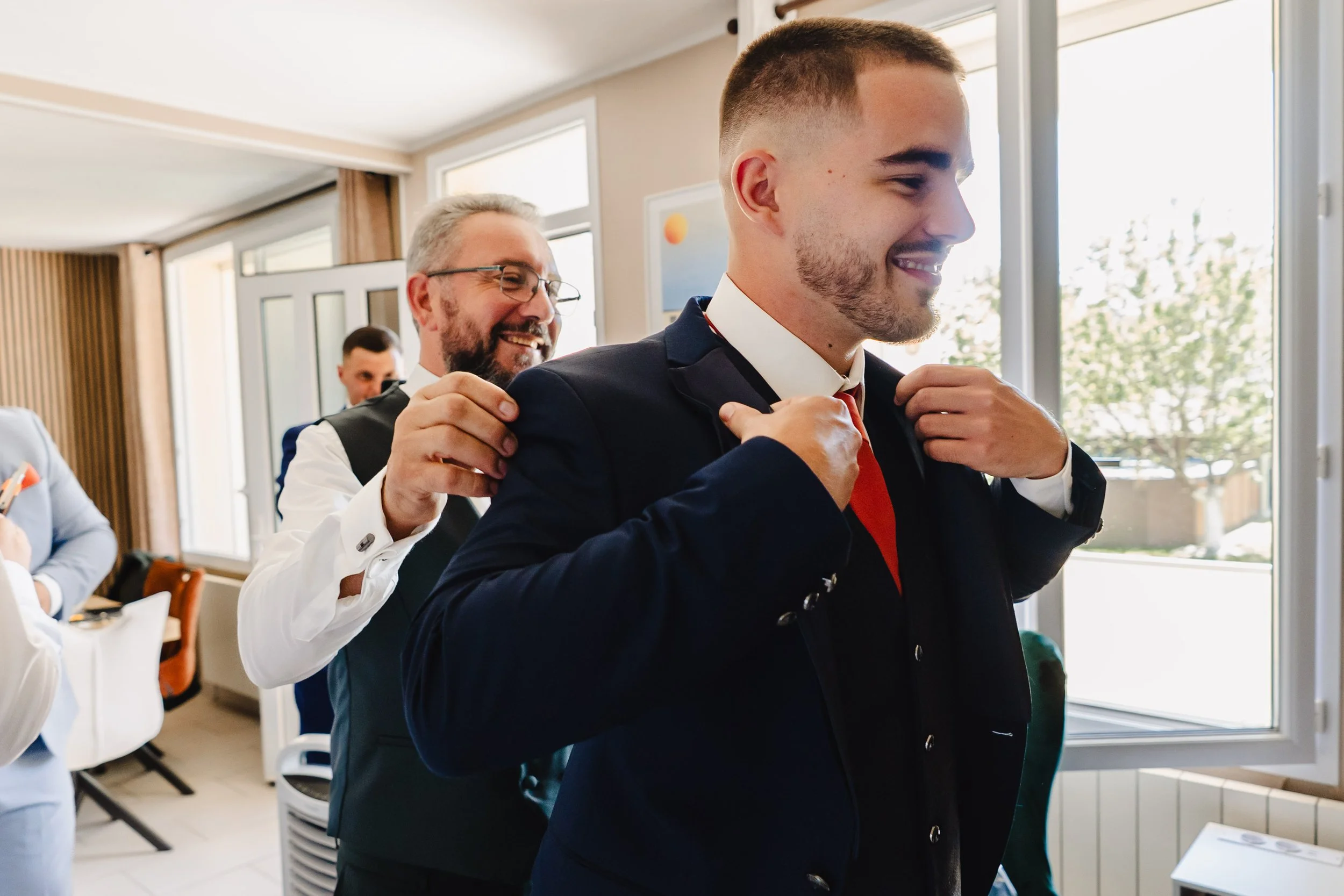 Un père aidant son fils, le marié à boutonner sa veste dans une pièce lumineuse