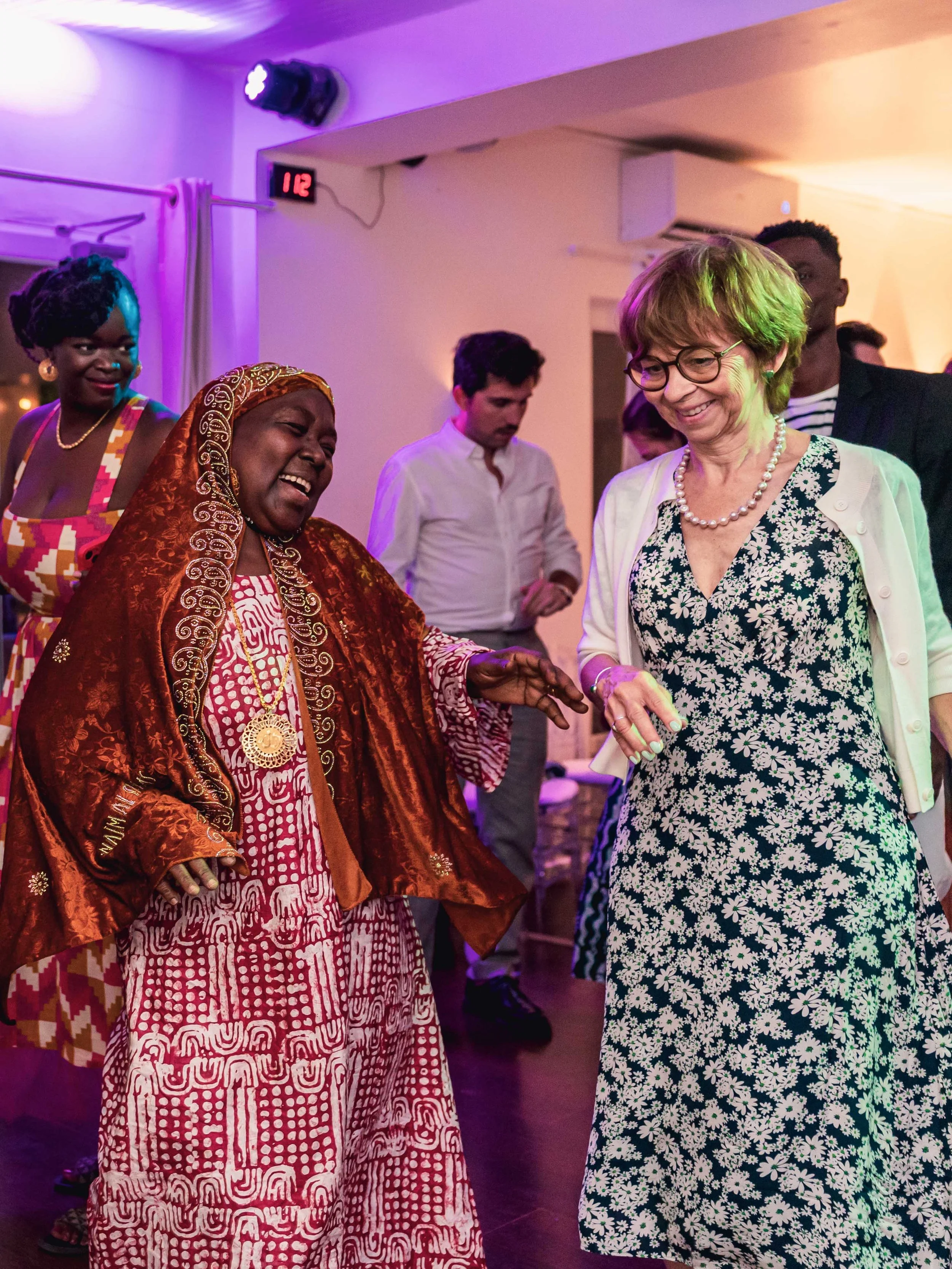 Groupe de personnes dansant et souriant lors d'une fête, ambiance colorée avec éclairage violet