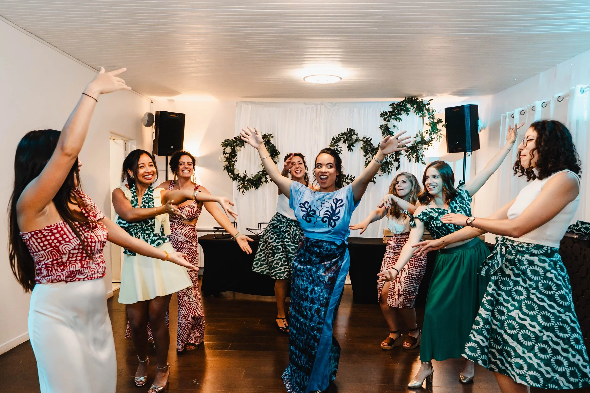 Groupe de femmes en vêtements colorés, dansant et souriant lors d'une fête ou d'une célébration à l'intérieur de la salle de réception du Moulin vert à Champigny.
