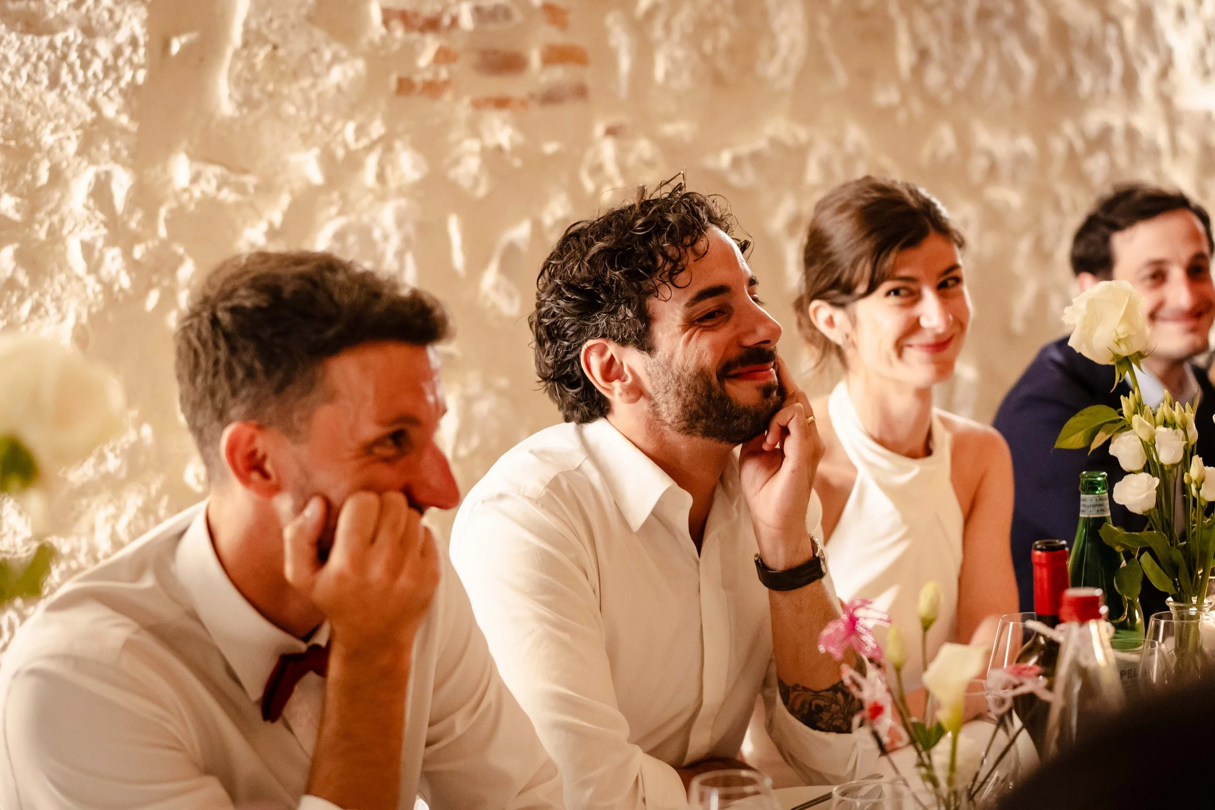 Gens assis à une table lors d'un repas ou d'une célébration, souriants et visiblement heureux, décor rétro avec murs texturés.