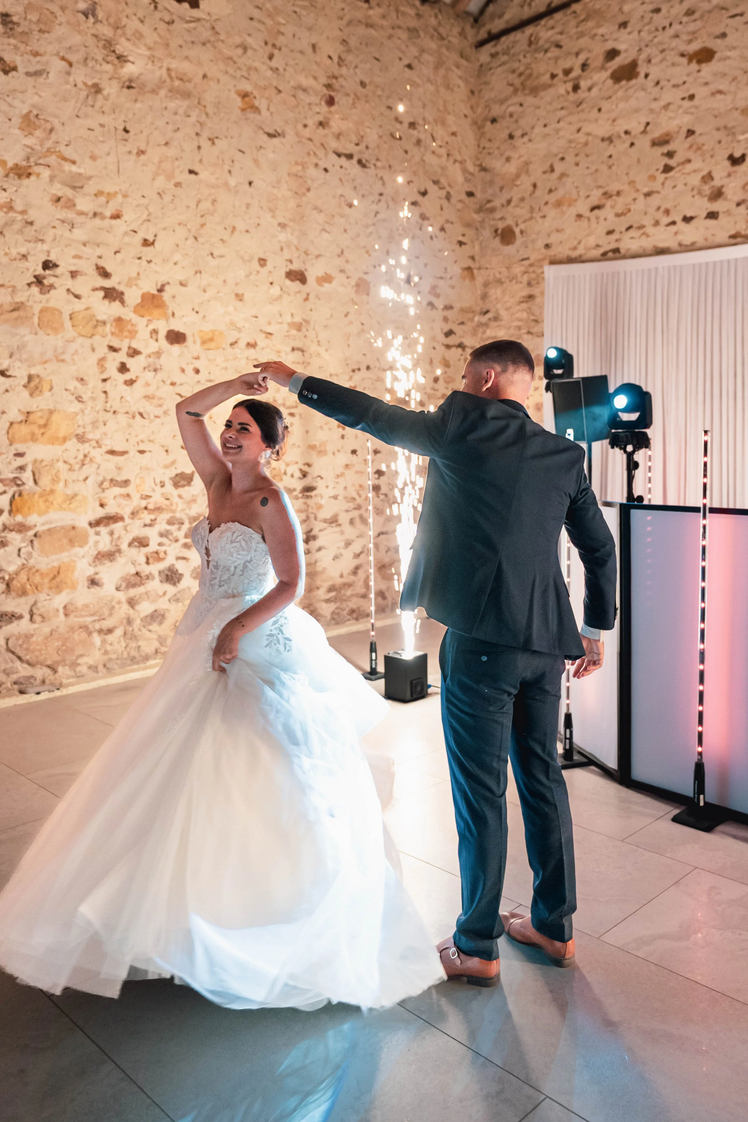 Un couple danse lors de leur mariage dans une salle avec mur en pierre.