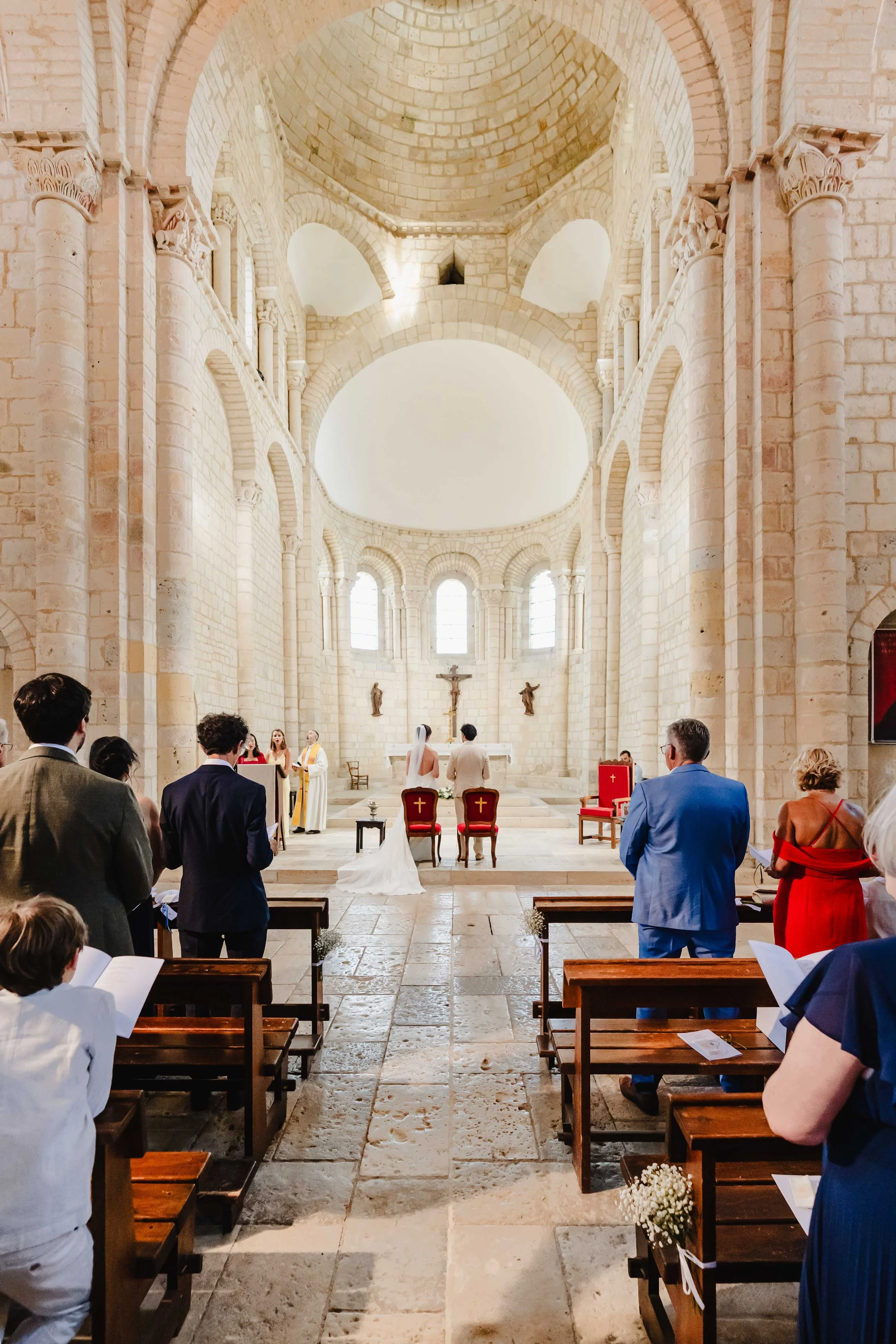 Cérémonie de mariage dans l'église de Moirax avec des invités assis, un couple près de l'autel, officiants et croix visible derrière eux.