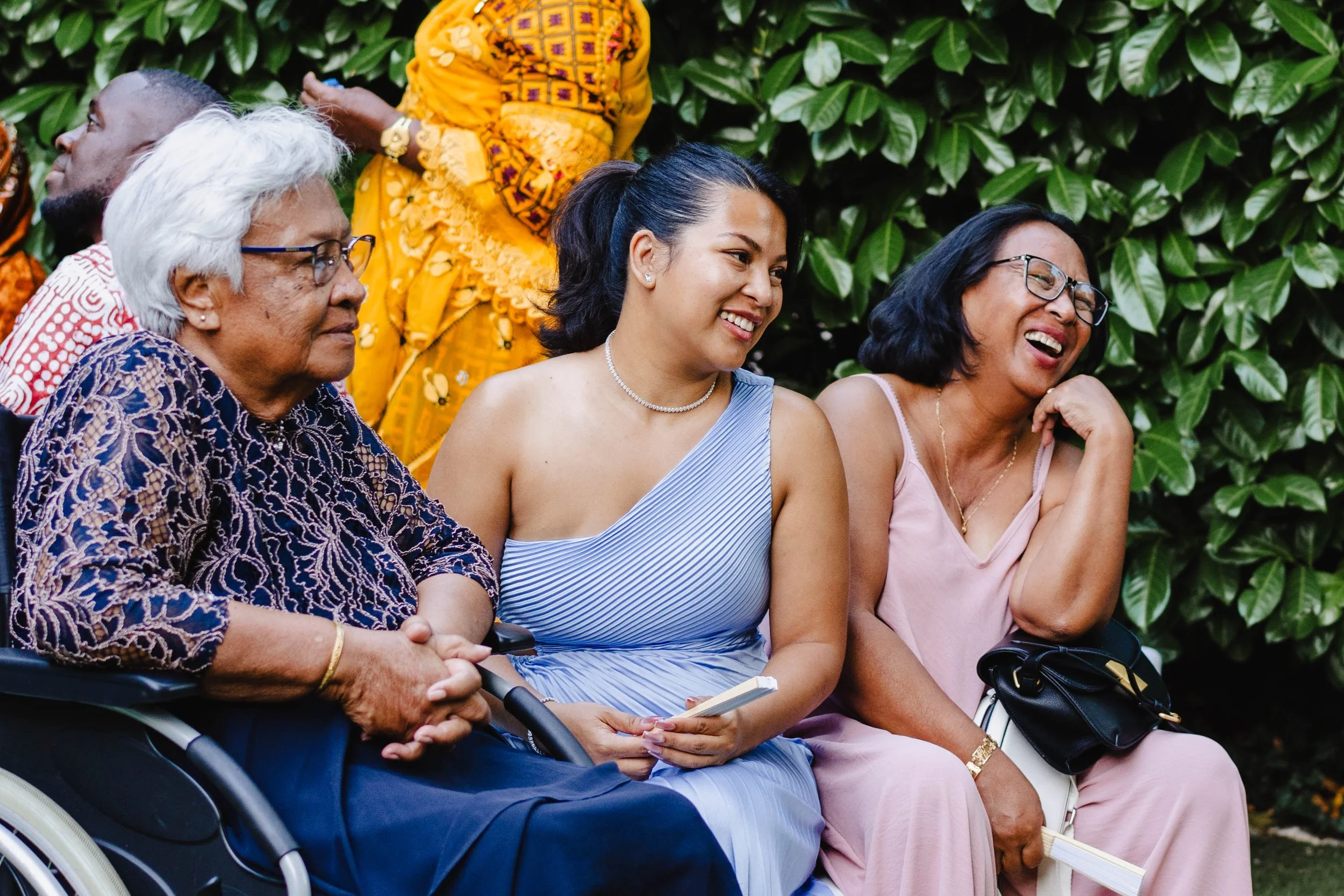 Trois femmes et un homme assis ensemble, souriants et riant, dans un jardin avec un arrière-plan de feuillage vert.