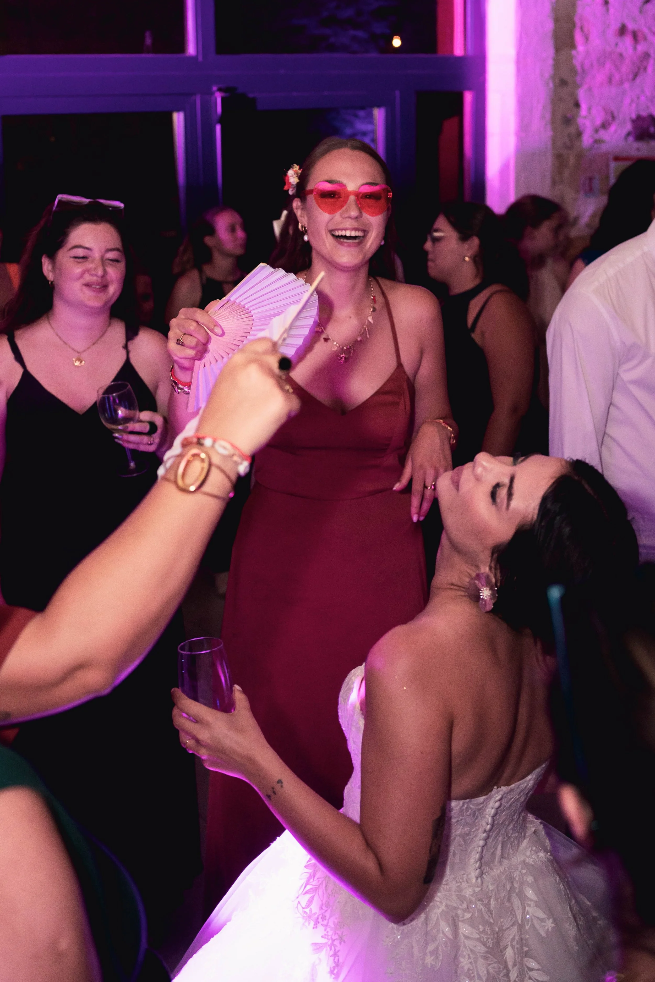 Un groupe de femmes souriantes lors d'une fête ou un mariage, avec des lumières roses et une ambiance festive.