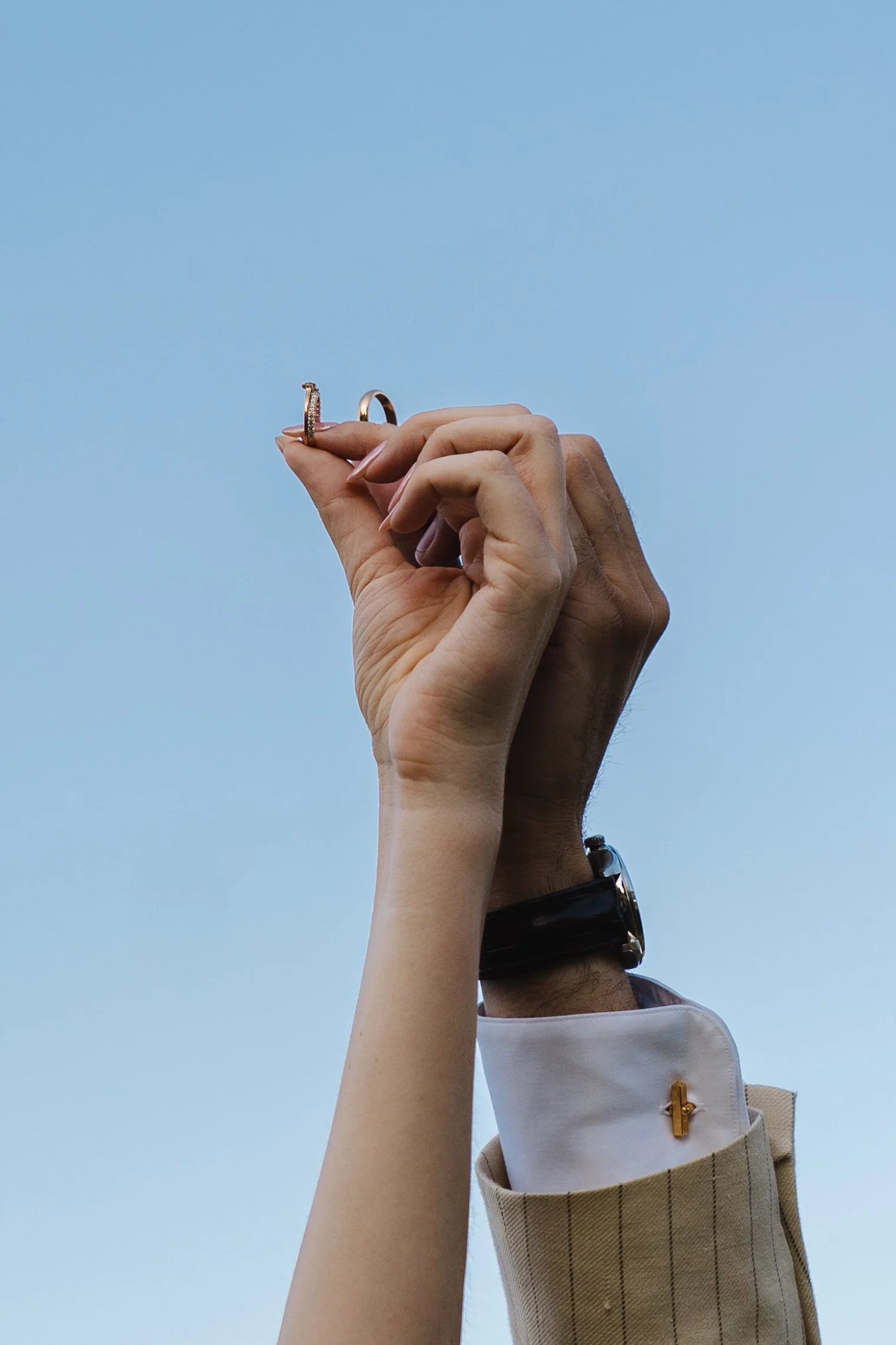 Deux mains, une masculine et une féminine, se croisent dans le ciel bleu, tenant des anneaux, symbolisant un mariage ou un engagement.