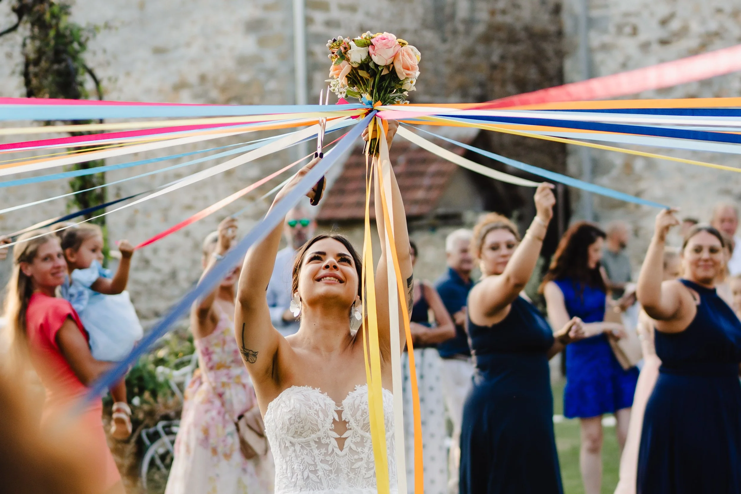 Une femme en robe blanche déposant un bouquet de fleurs au centre d'une cérémonie avec des invités, lors d'une fête ou d'un mariage au domaine de Mauperthuis.
