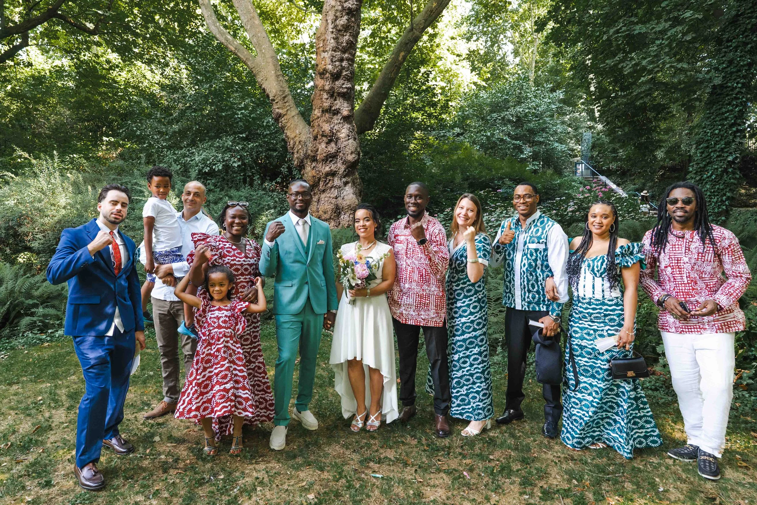 groupe de personnes devant un grand arbre, certaines portant des tenues traditionnelles et d'autres en vêtements de fête, posant pour une photo dans un cadre naturel au parc de Bercy