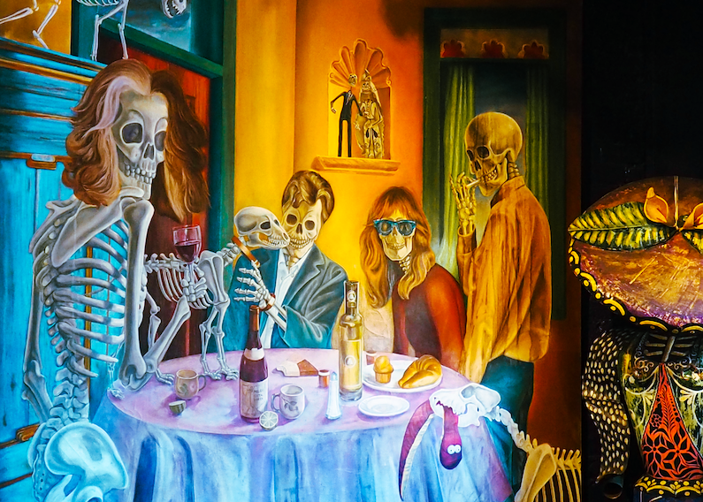 A vibrant painting of skeletons and a person with a skeleton face enjoying a meal at a dining table, with colorful background and decorative elements.
