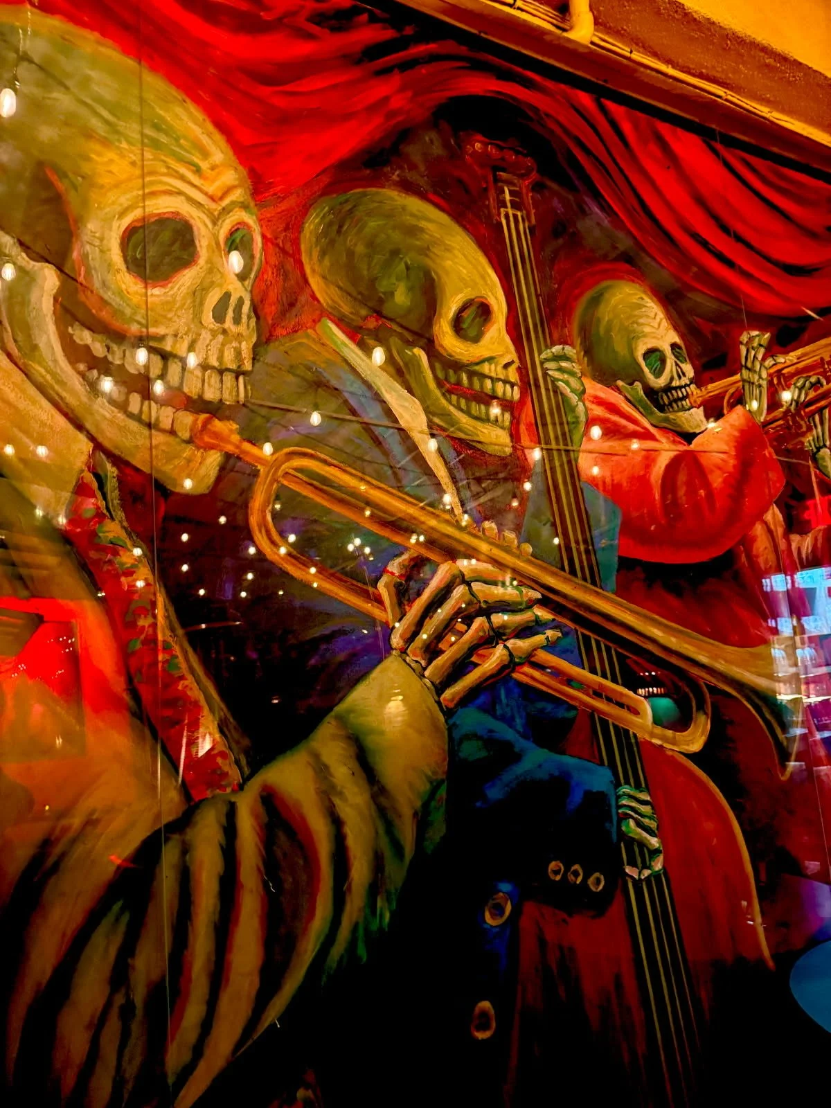 Colorful mural of skeletons playing musical instruments, with a skeleton in the foreground playing a trumpet, and others playing a double bass and violin, set against a vibrant red background.