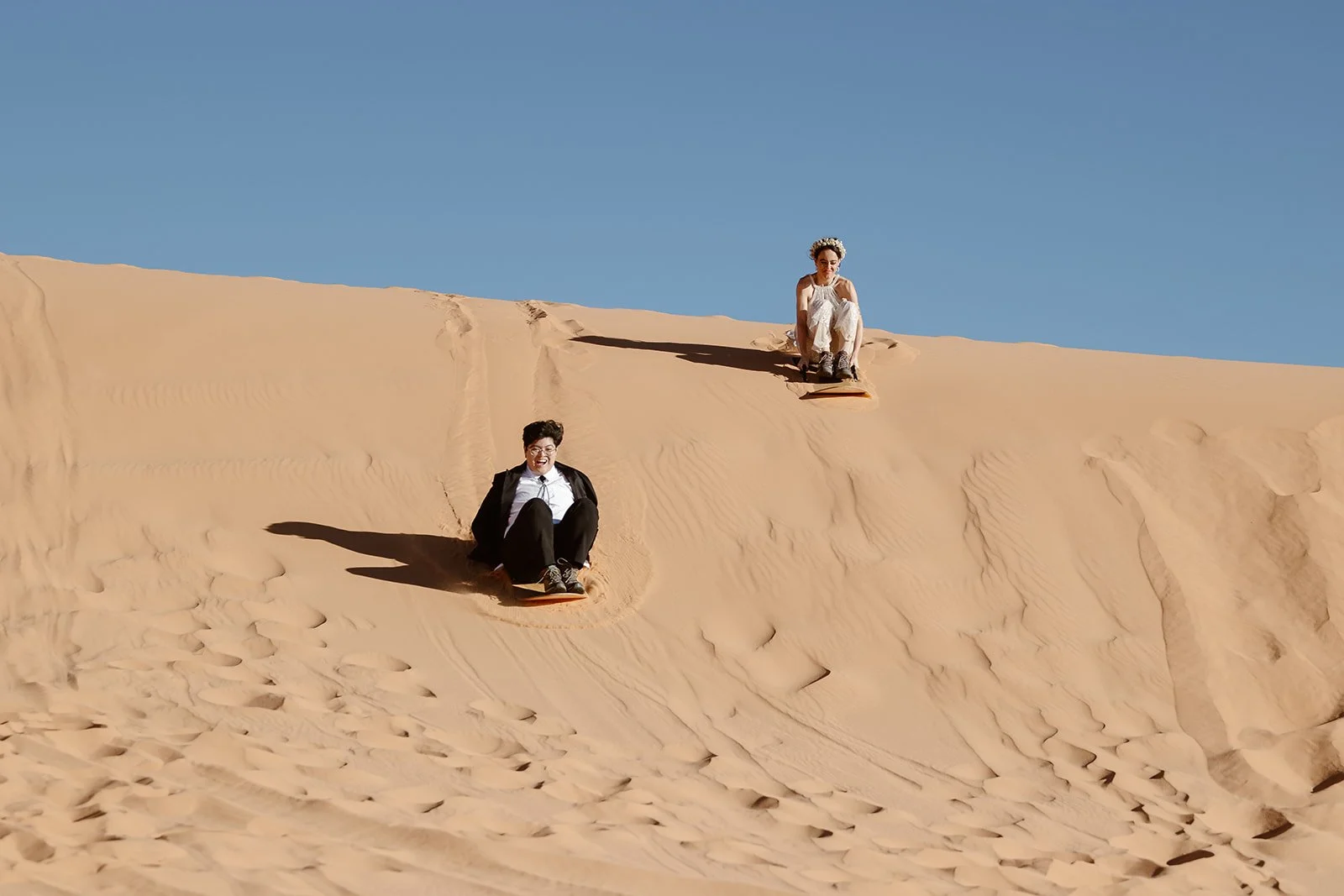 pager arizona elopement couple going down sand dune on sandboards