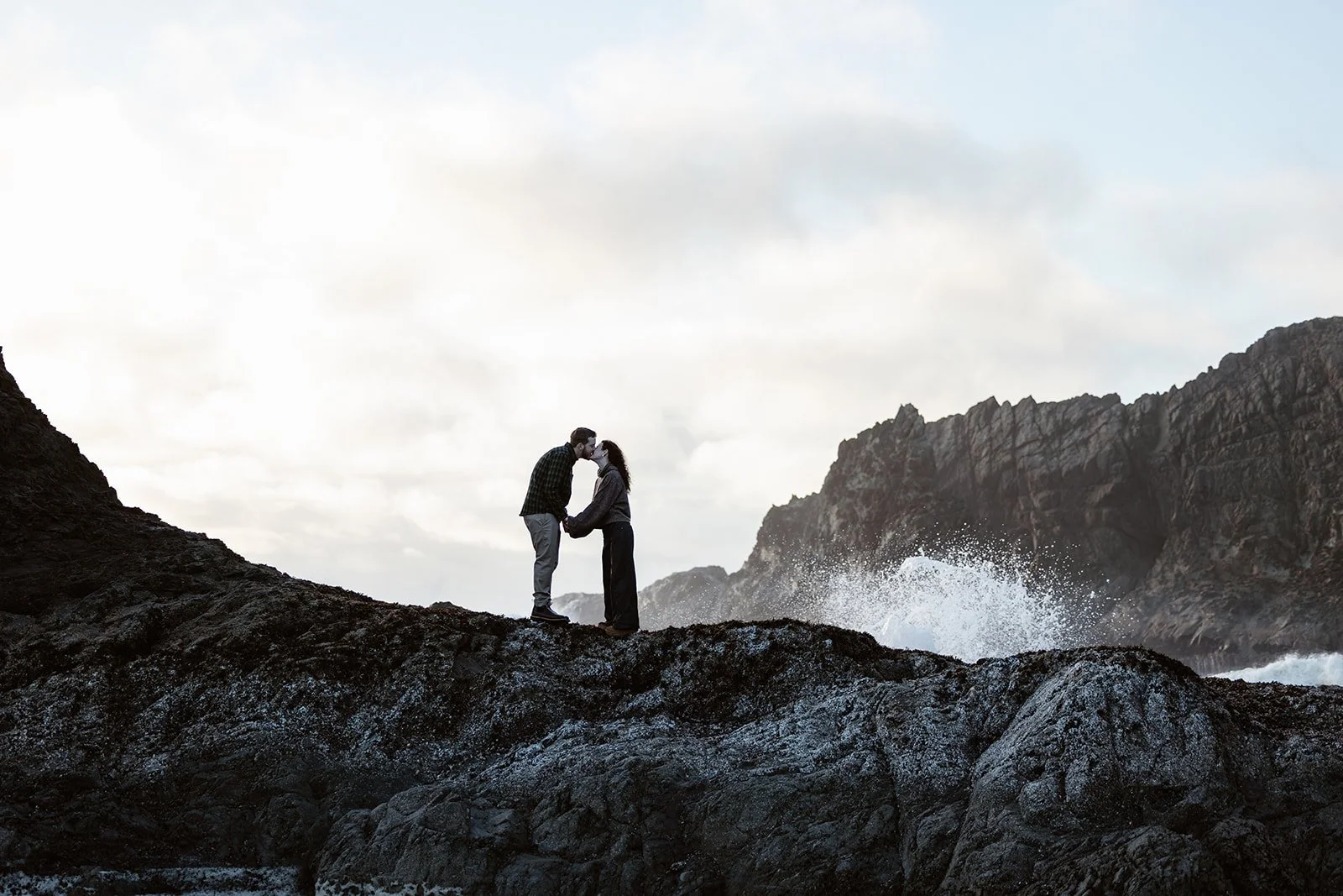 surprise engagement couple kissing on the washington coast on a rock