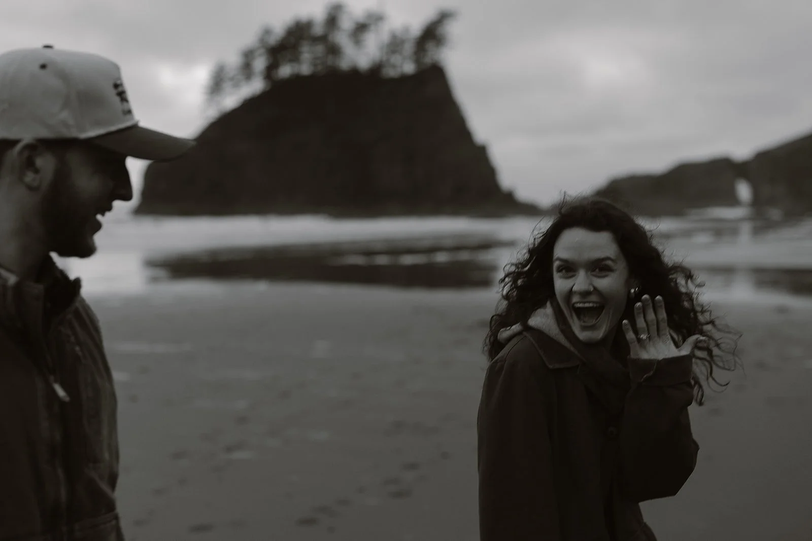 woman holding hand up after saying yes during her surprise engagement on the wa coast