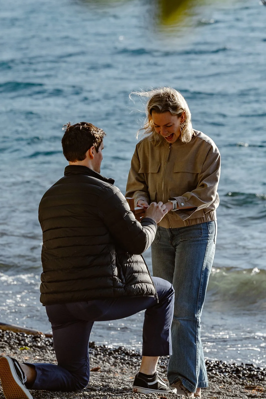 couple smiling while fiance is putting ring on hand for surprise proposal at lake crescent