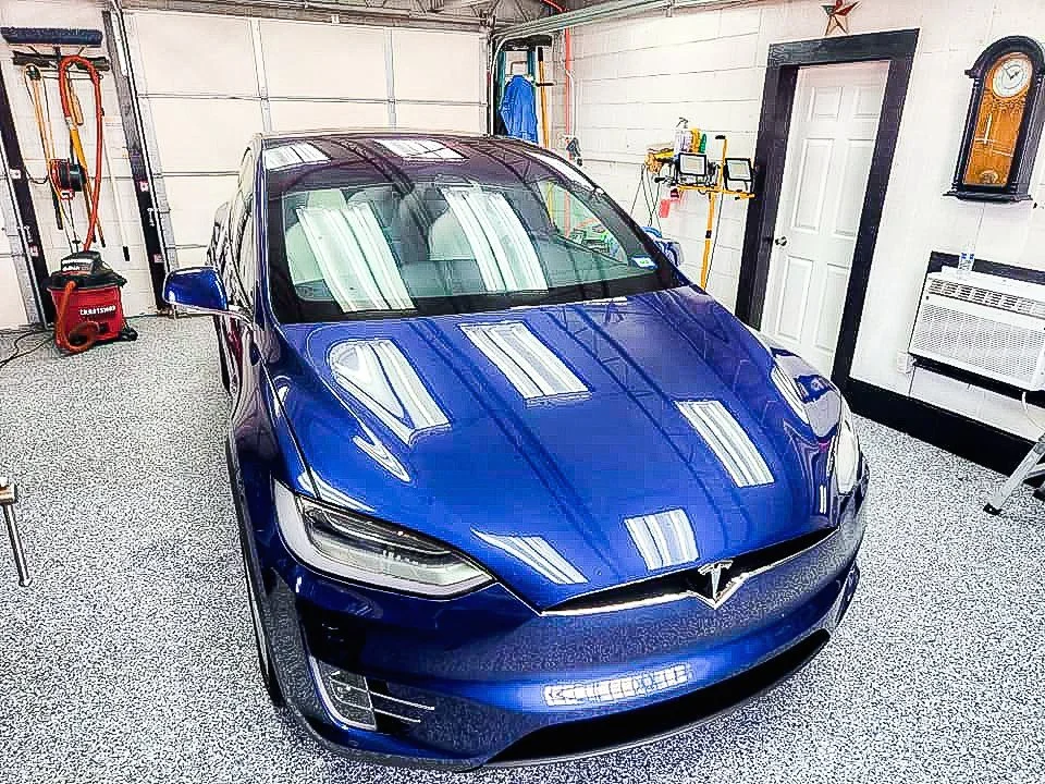 Blue Tesla parked inside a garage with various tools and equipment on the walls.