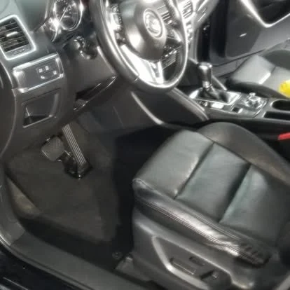 Interior of a car showing the driver's seat, steering wheel, gear shift, and pedals.