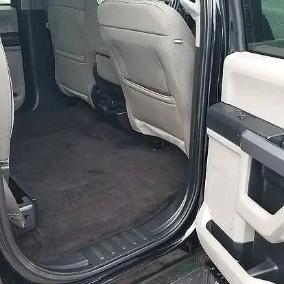 View of the interior of a vehicle showing the back seat area with beige seats and an empty black carpeted floor.