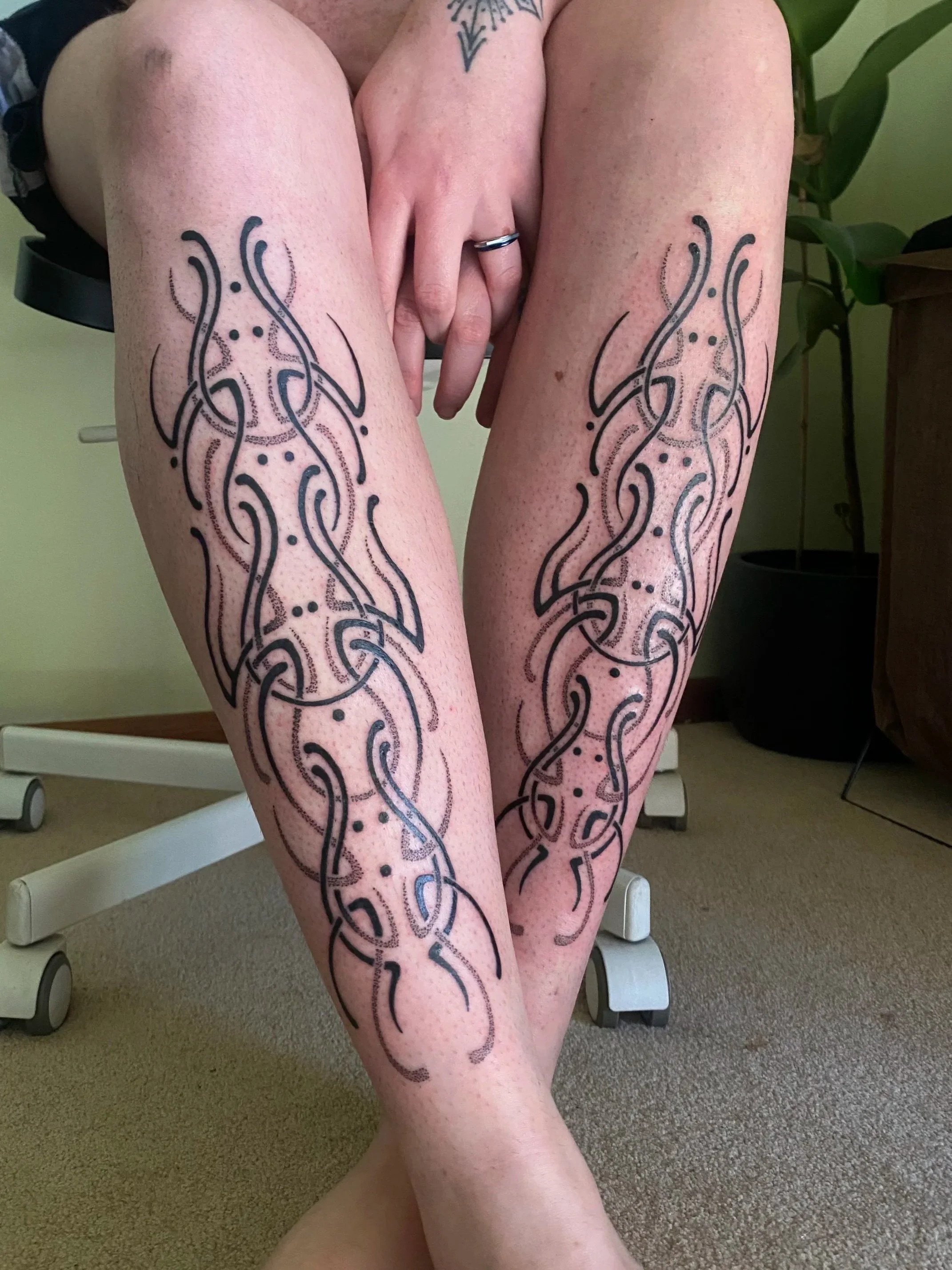 displaying intricate black tribal-style tattoos on their shins. The tattoos feature swirling lines and dots.