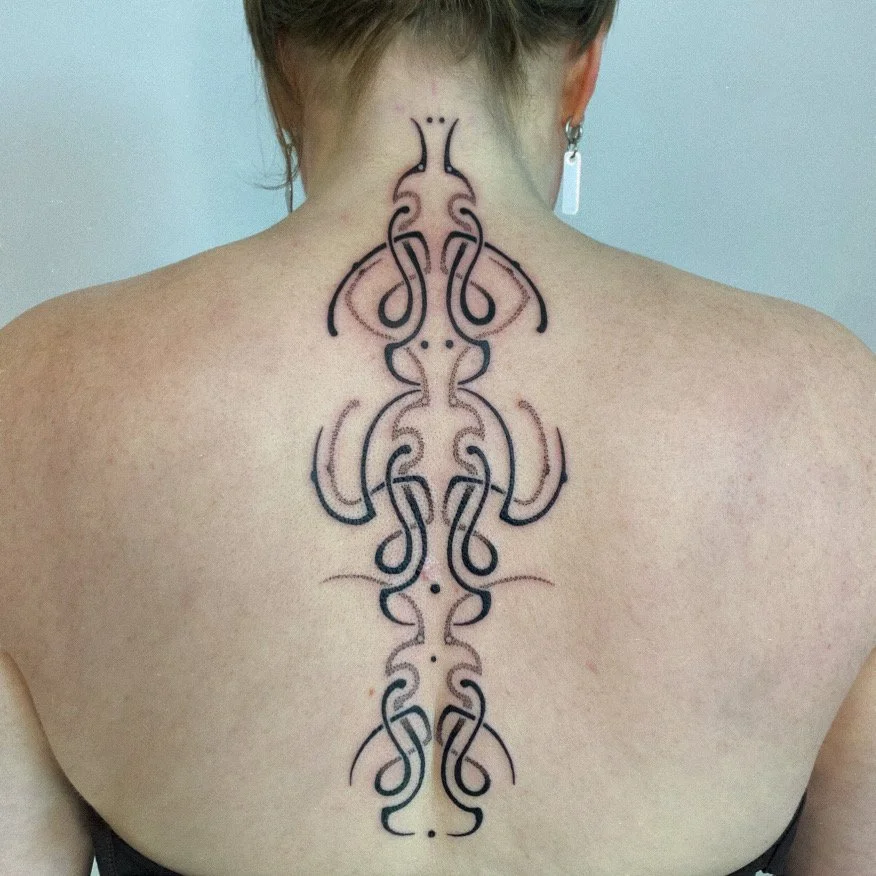 Tattoo of symmetrical, abstract black line designs on a person's back, extending from the neck to the middle of the back.