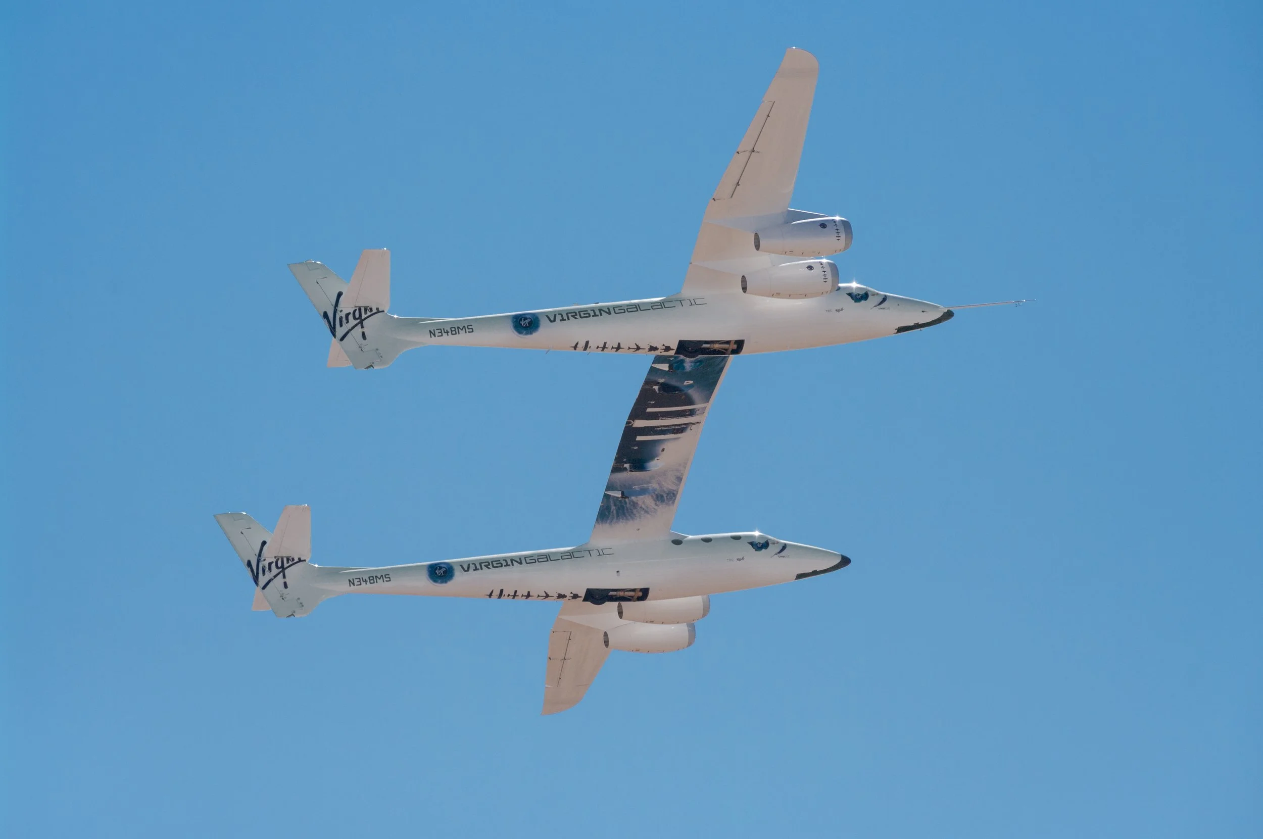 Virgin Galactic WhiteKnightTwo carrying SpaceShipTwo in flight against a clear blue sky.